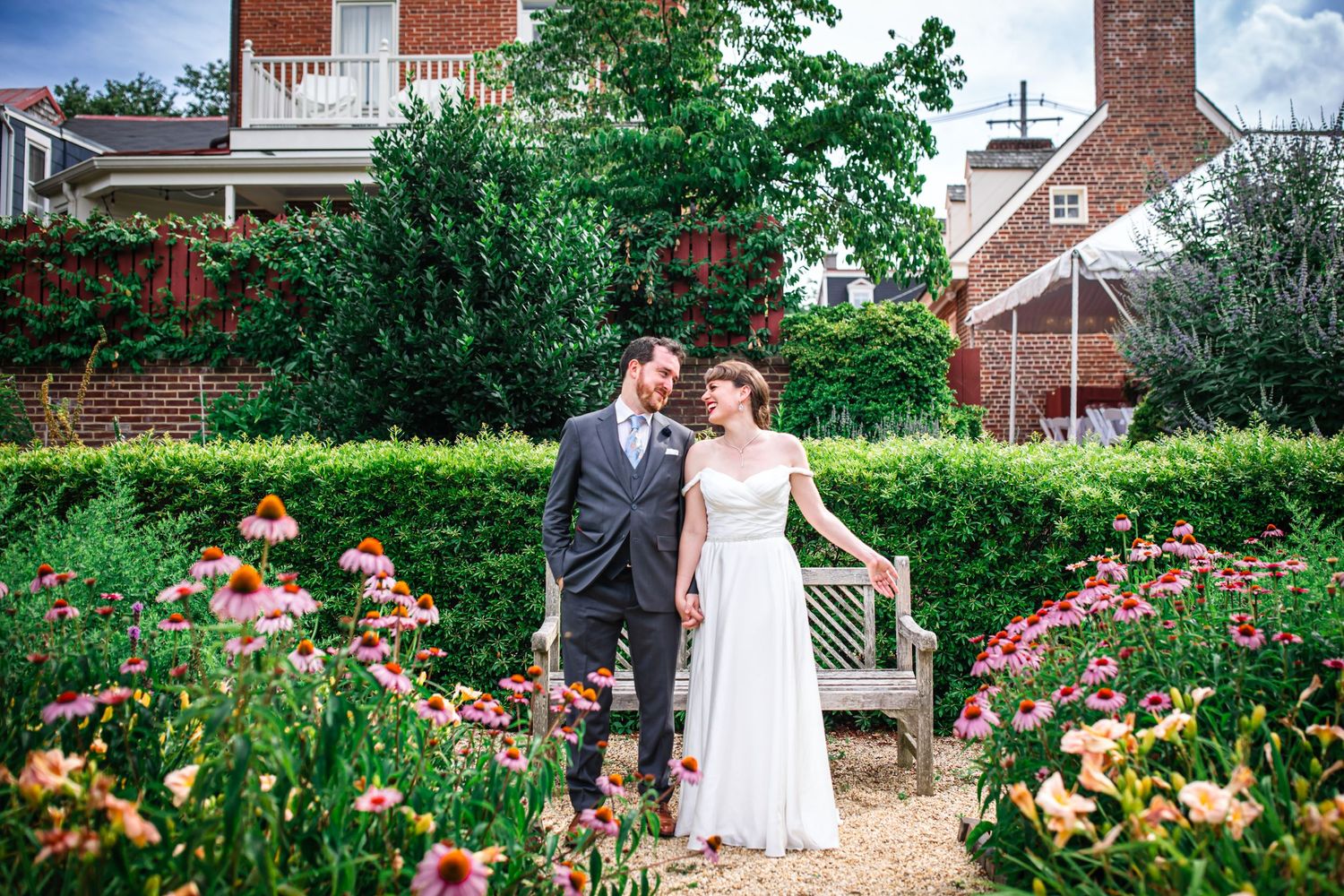 Romantic garden portrait with blooming flowers and red brick house in background.