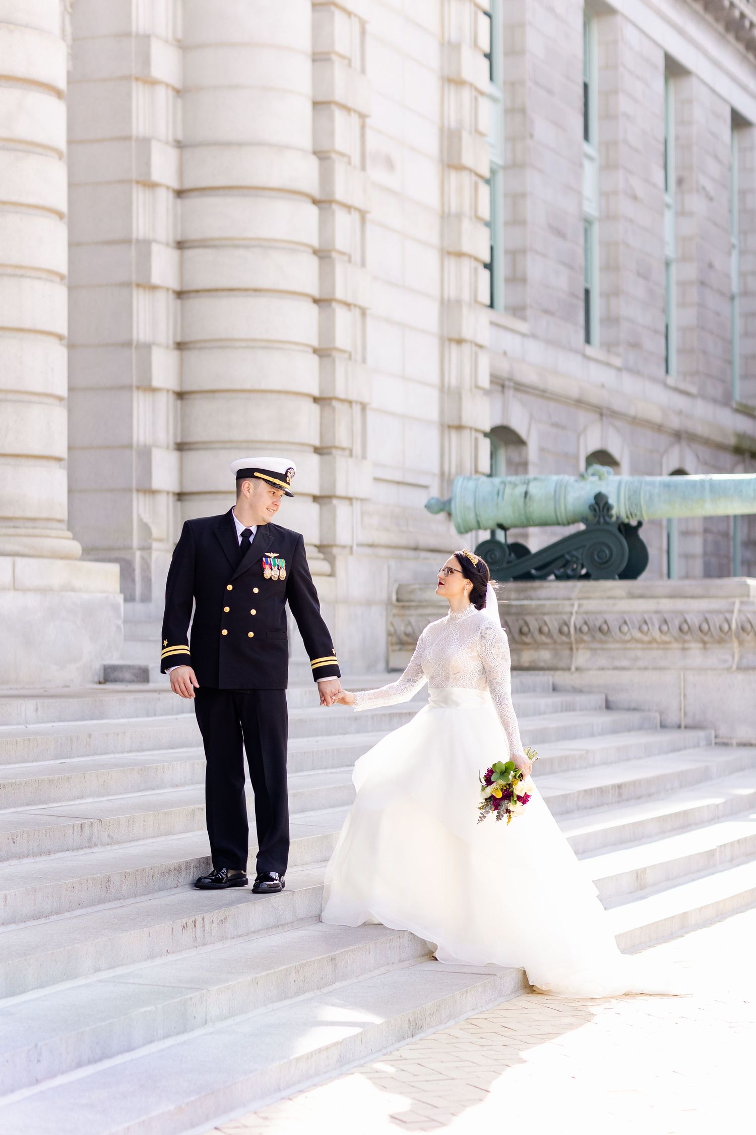 Wedding couple posing on grand white stone steps with decorative columns and architecture.
