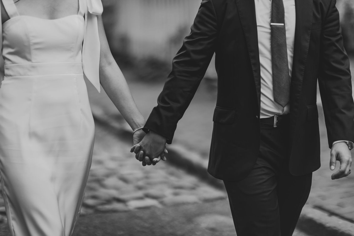 Black and white close-up of couple holding hands while walking in formal attire.