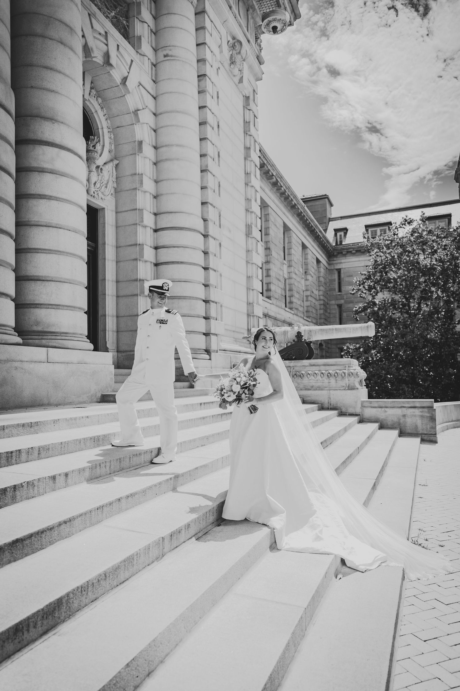 Black and white wedding photo on grand architectural steps with flowing dress and veil.