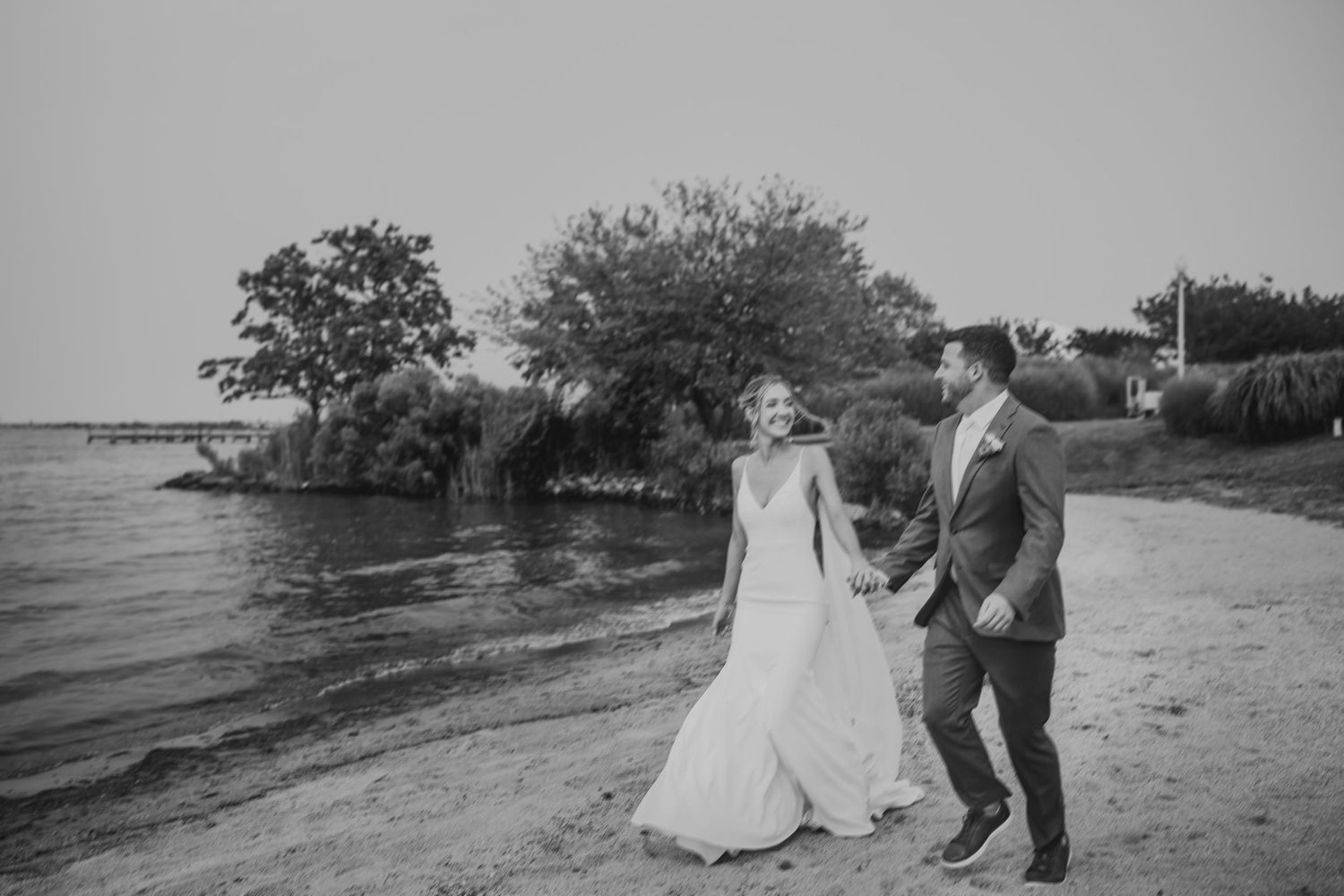 Black and white beach wedding portrait with trees and water in background.