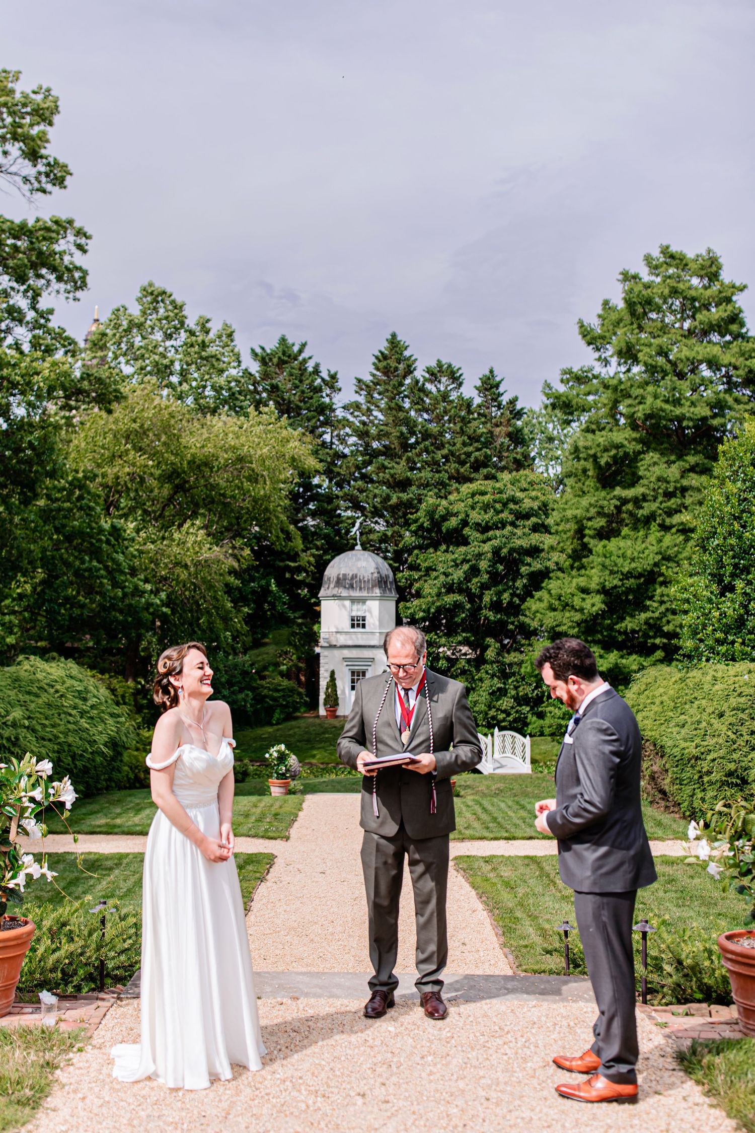 Outdoor garden wedding ceremony setup with white chairs and gazebo surrounded by greenery.