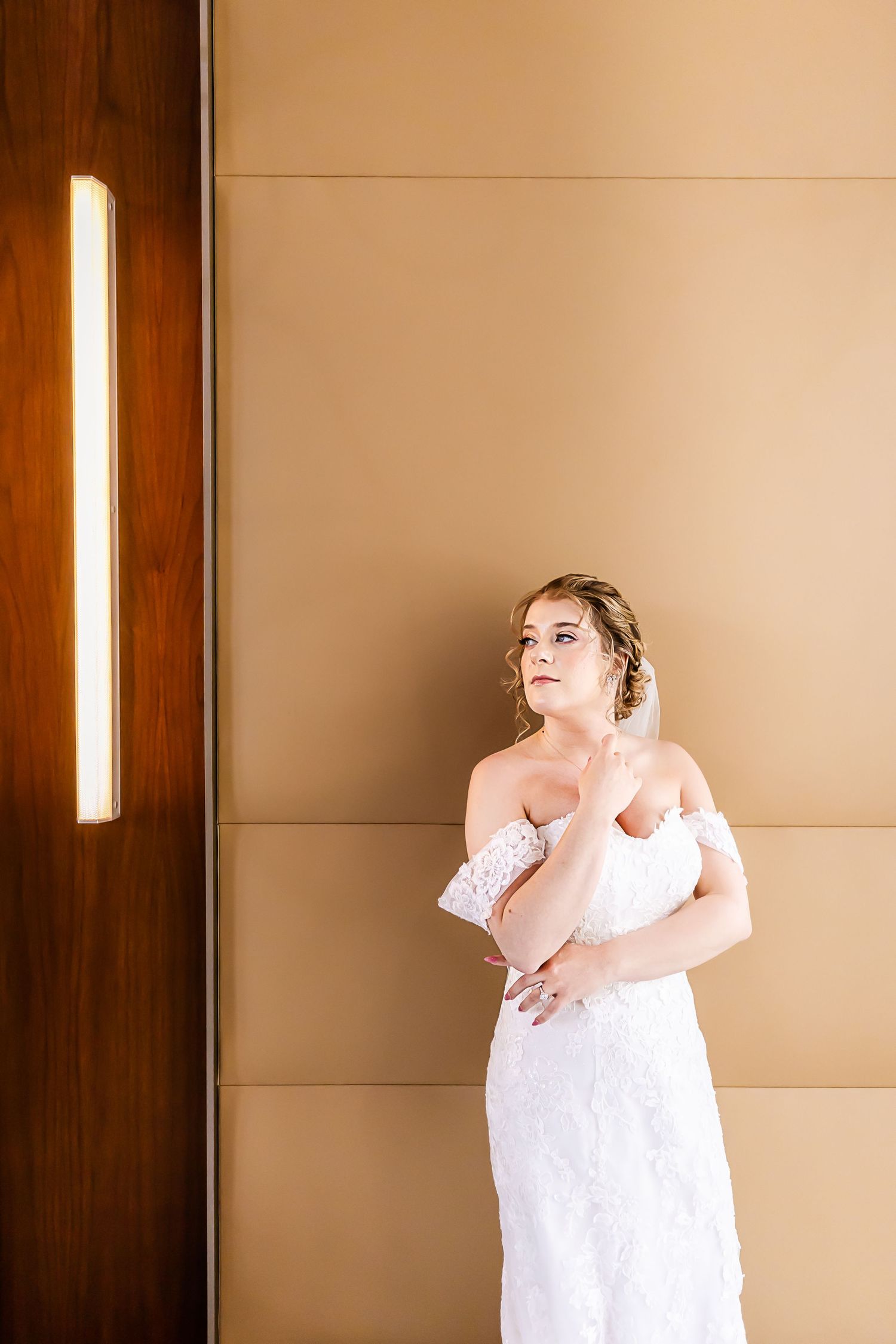 Elegant bridal portrait against minimalist beige wall with dramatic lighting.
