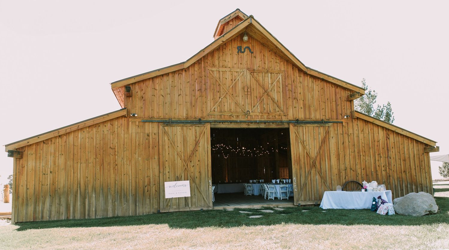 Rustic wooden barn venue with large open doors set against a light pink sky.