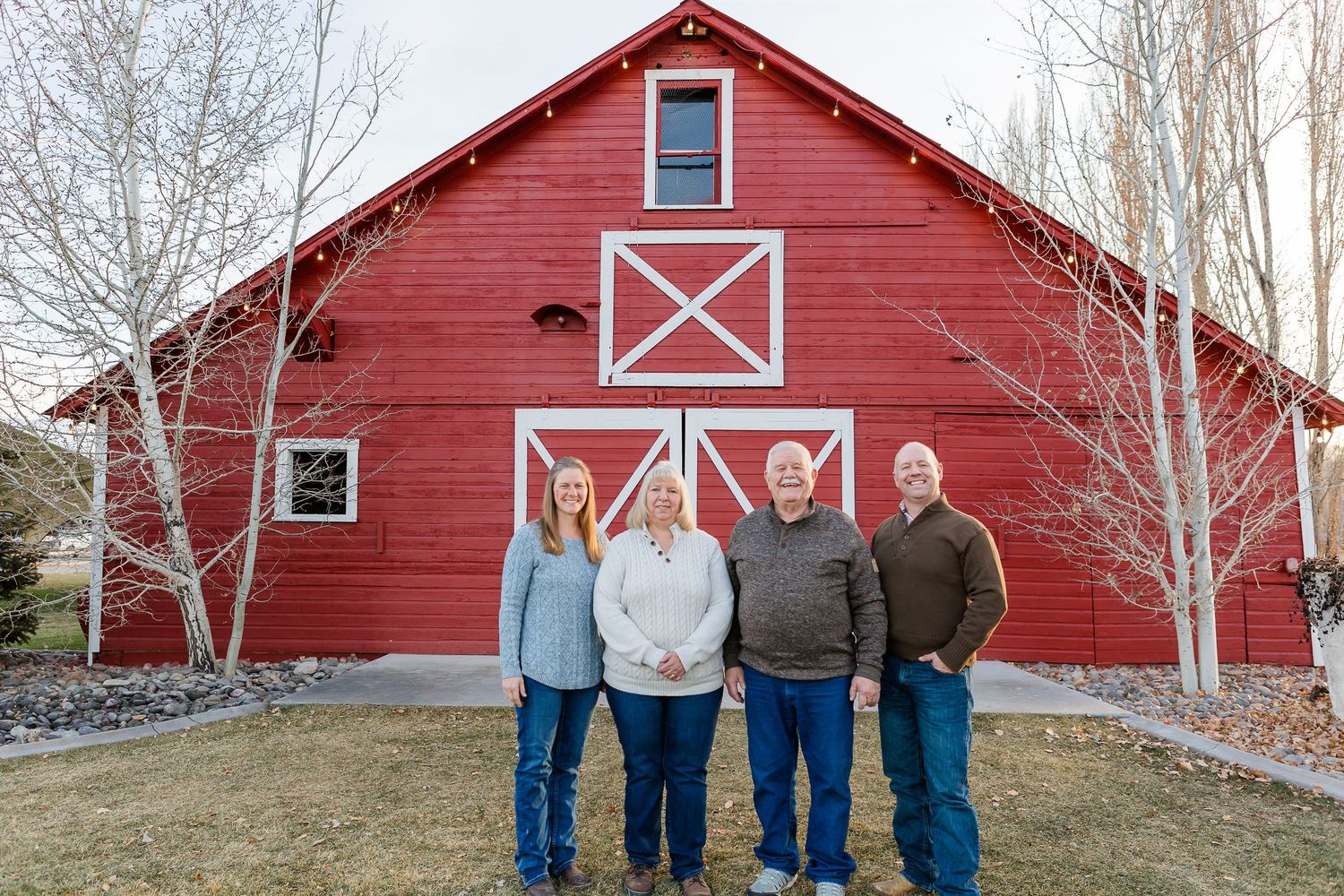 A small group stands against a red barn with distinctive white X patterns on its facade.