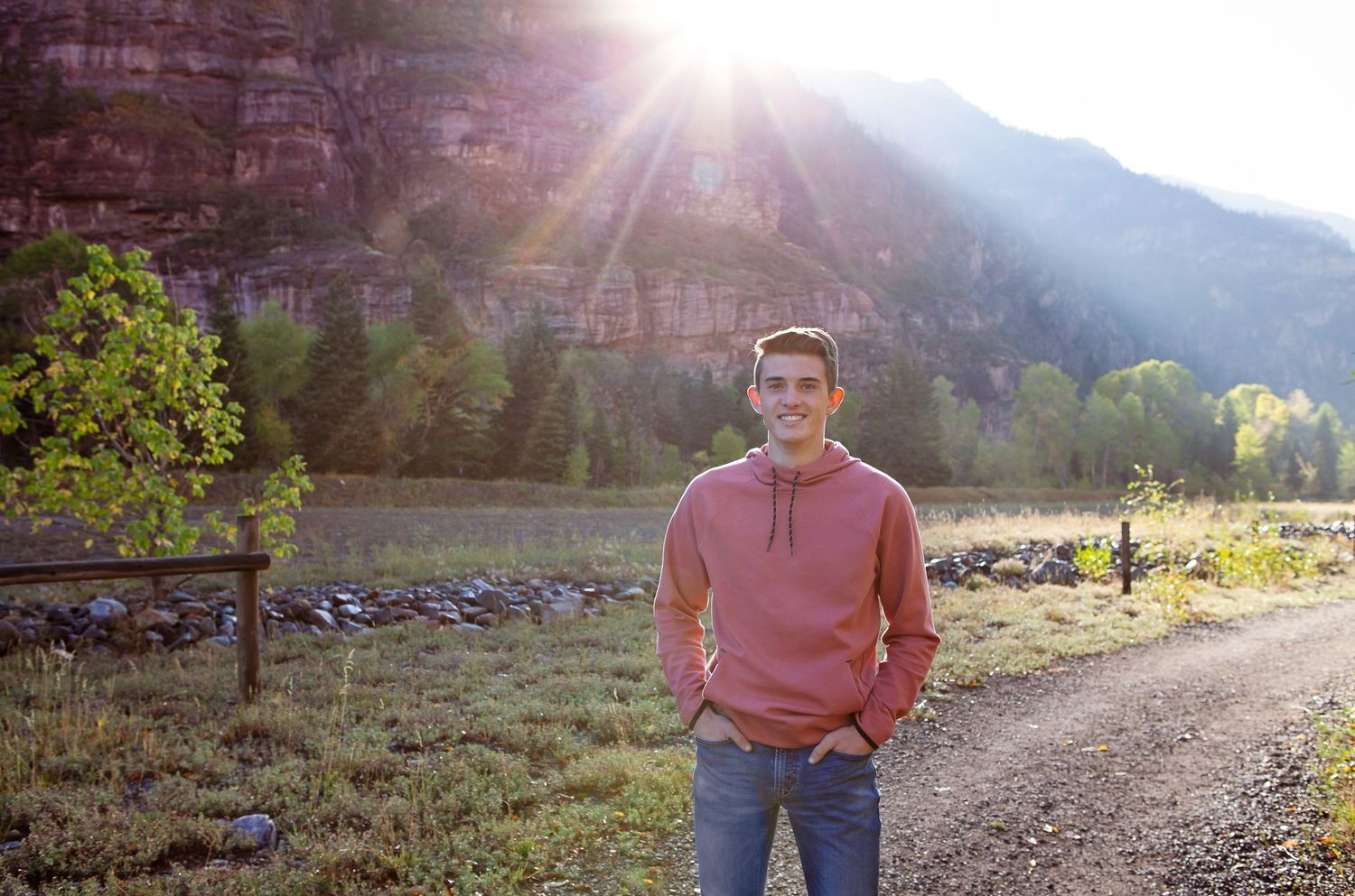 A person in casual wear stands on a trail with sunlit red cliffs in background.