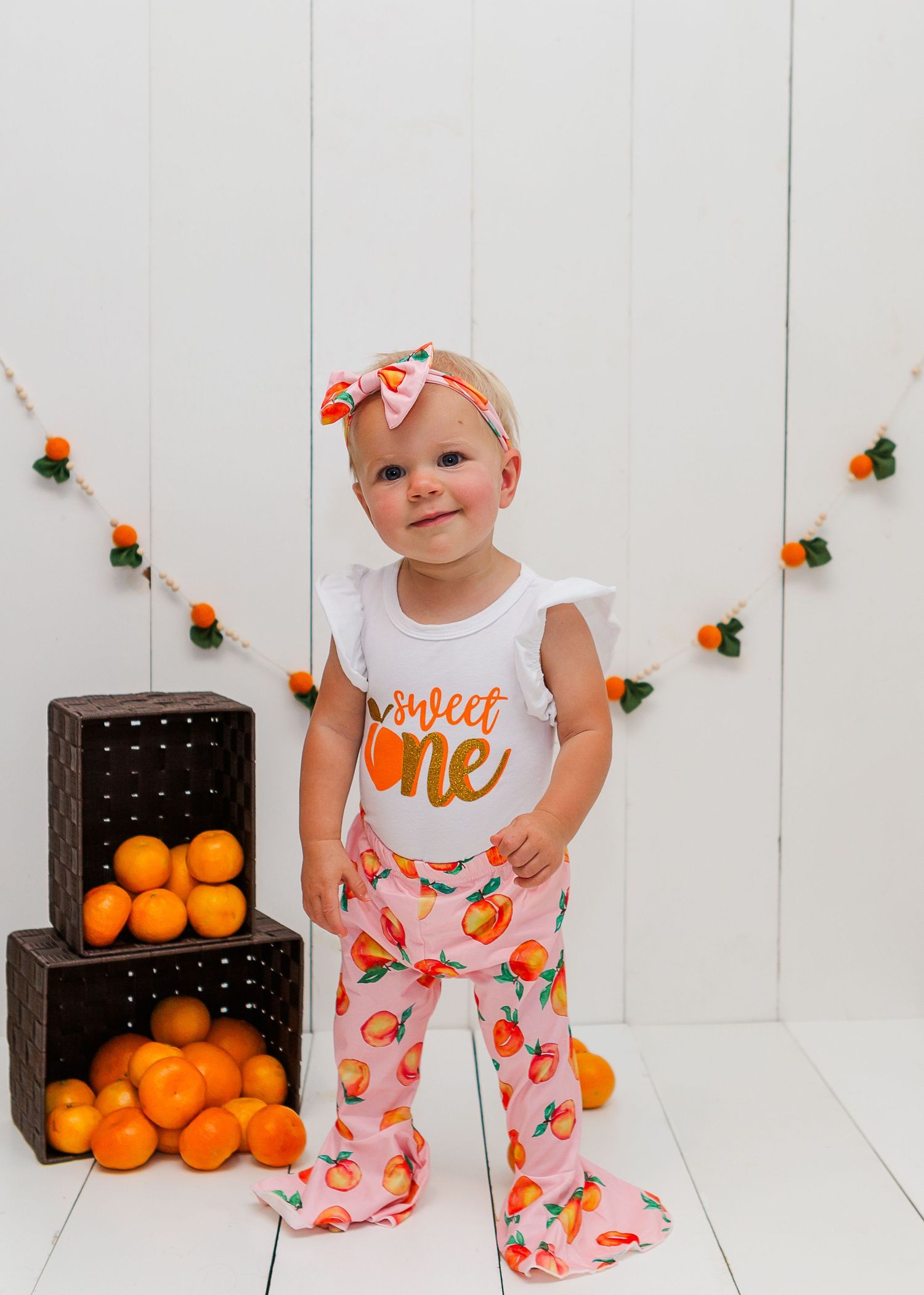White and orange citrus-themed outfit with pumpkins and string lights in background.