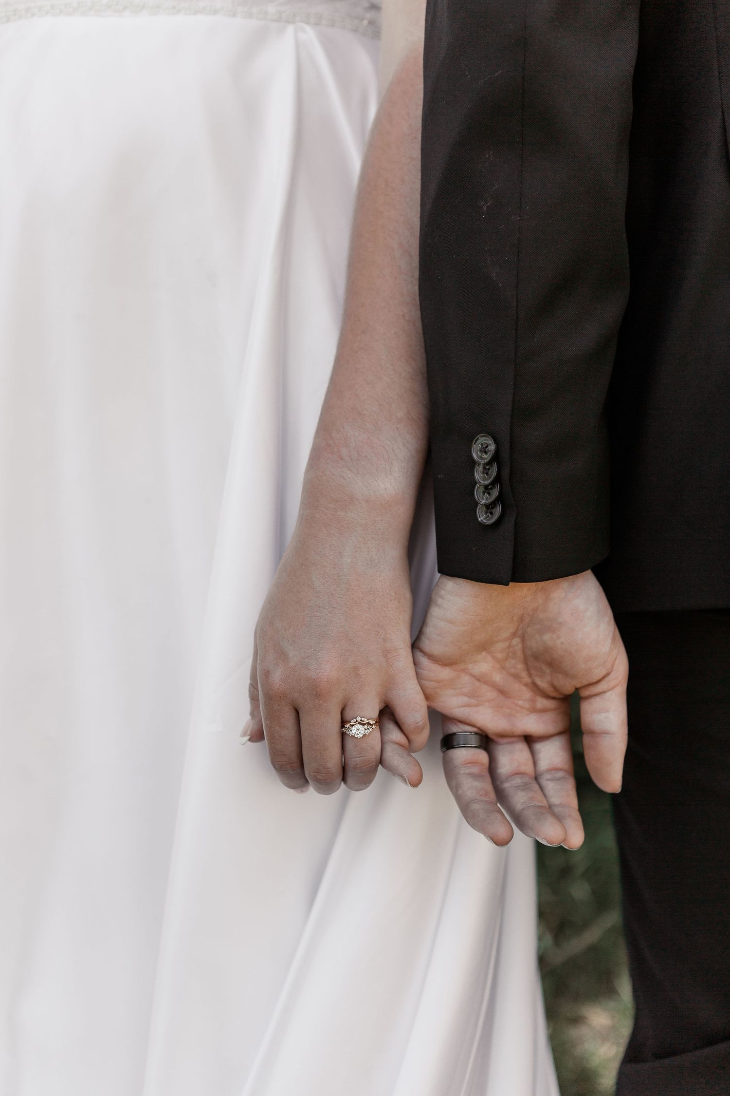A close-up detail shot of hands and wedding dress fabric showing a sparkling engagement ring.