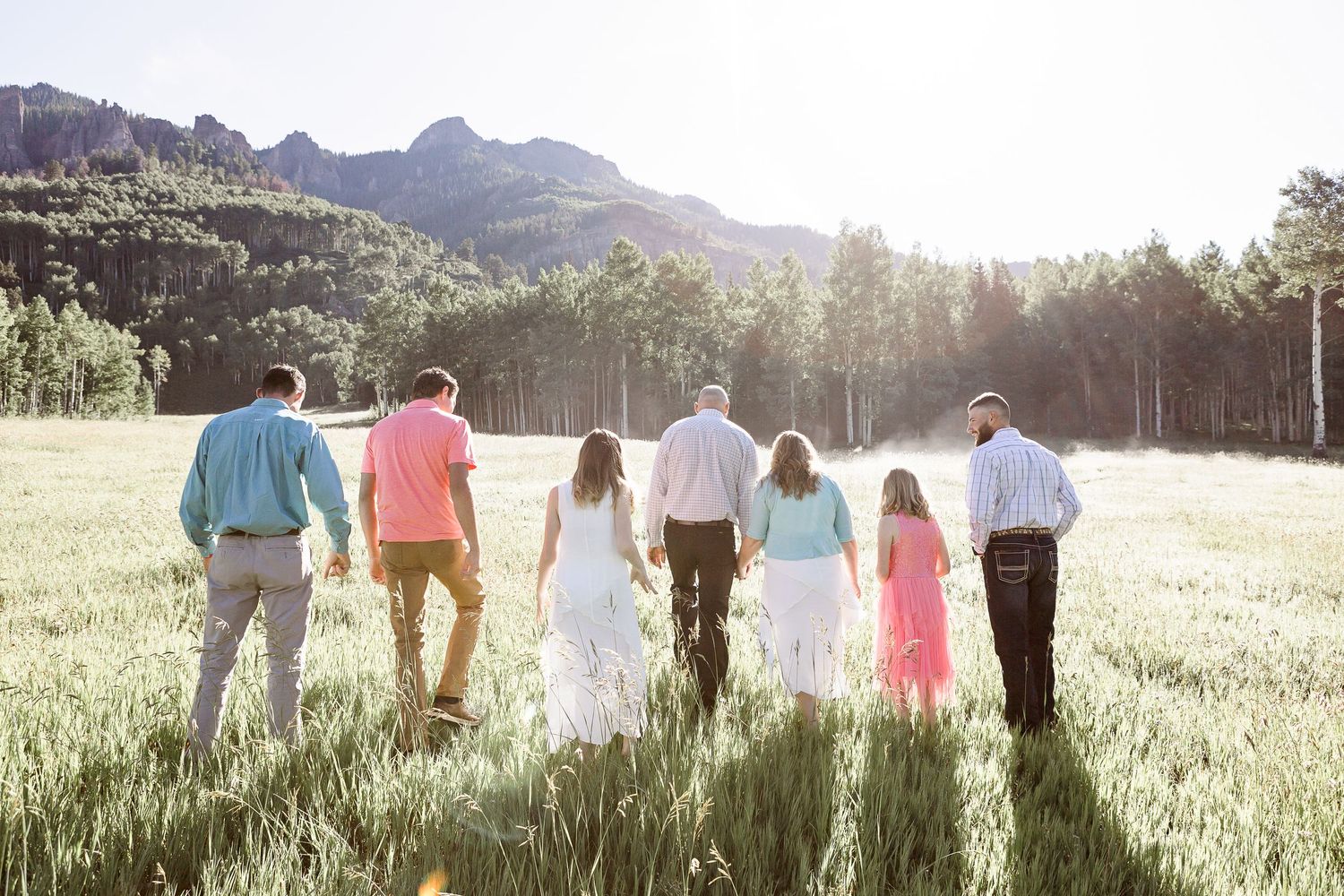 Group walks through sunlit mountain meadow with dramatic peaks in background.