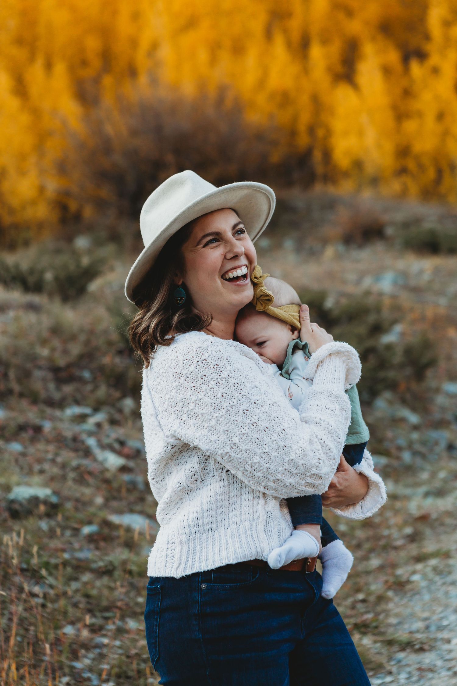 A joyful moment outdoors with a white sweater and hat against golden autumn foliage in the background.