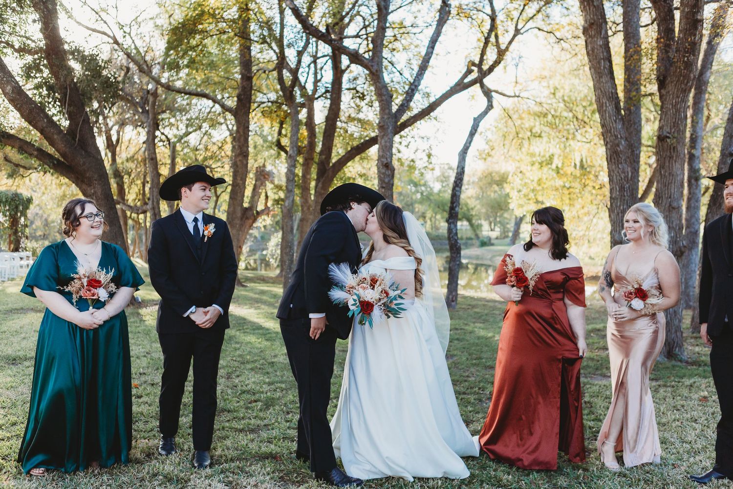 Wedding party poses outdoors in formal attire with bridesmaids in jewel-toned dresses.