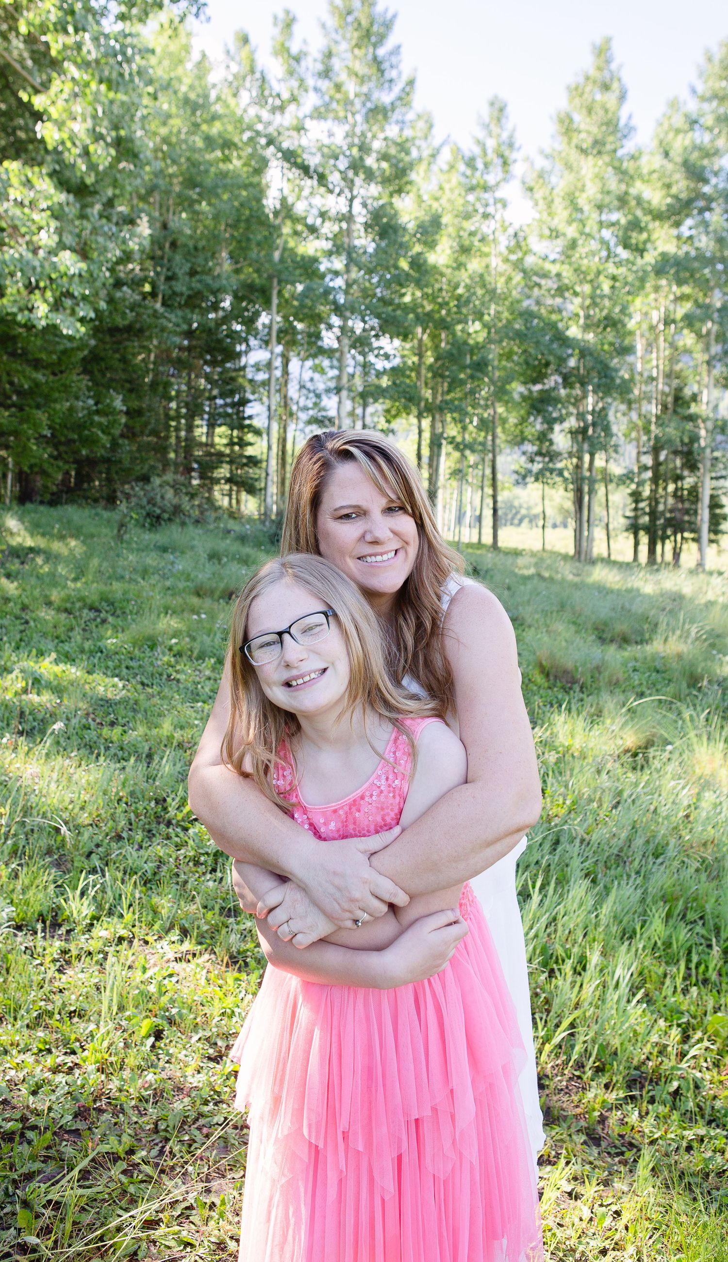 Tender embrace captured in sunny mountain meadow with pine forest backdrop.
