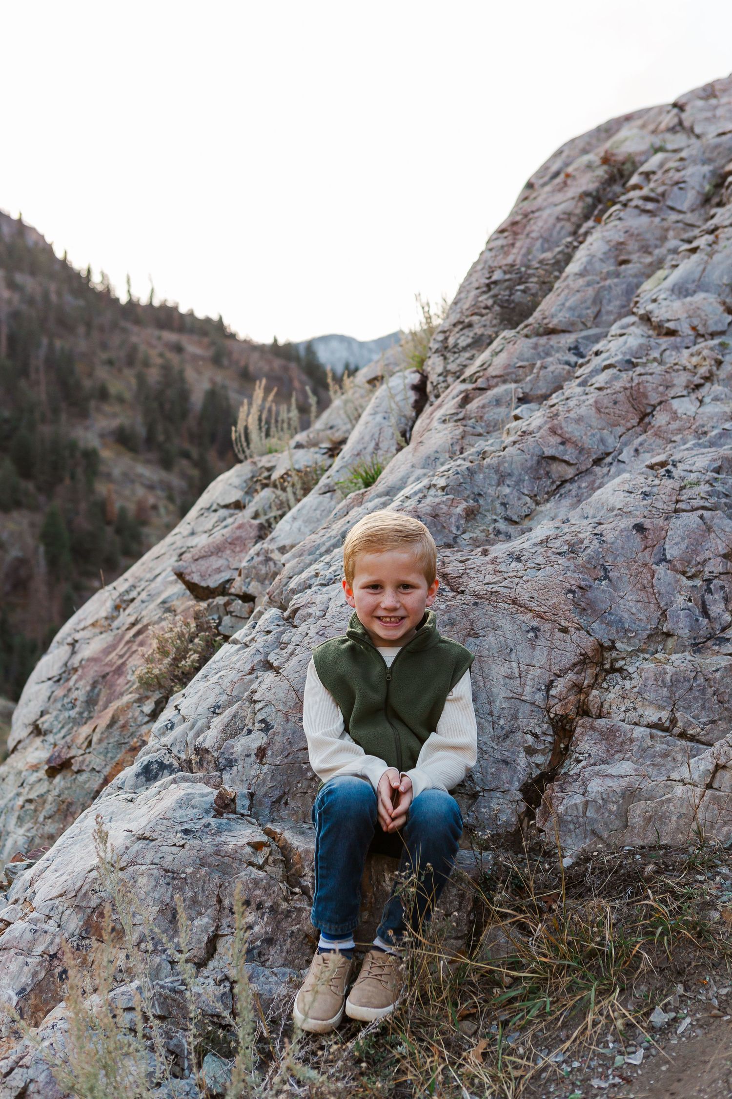 Young child sitting on rocky mountainside wearing casual fall attire.