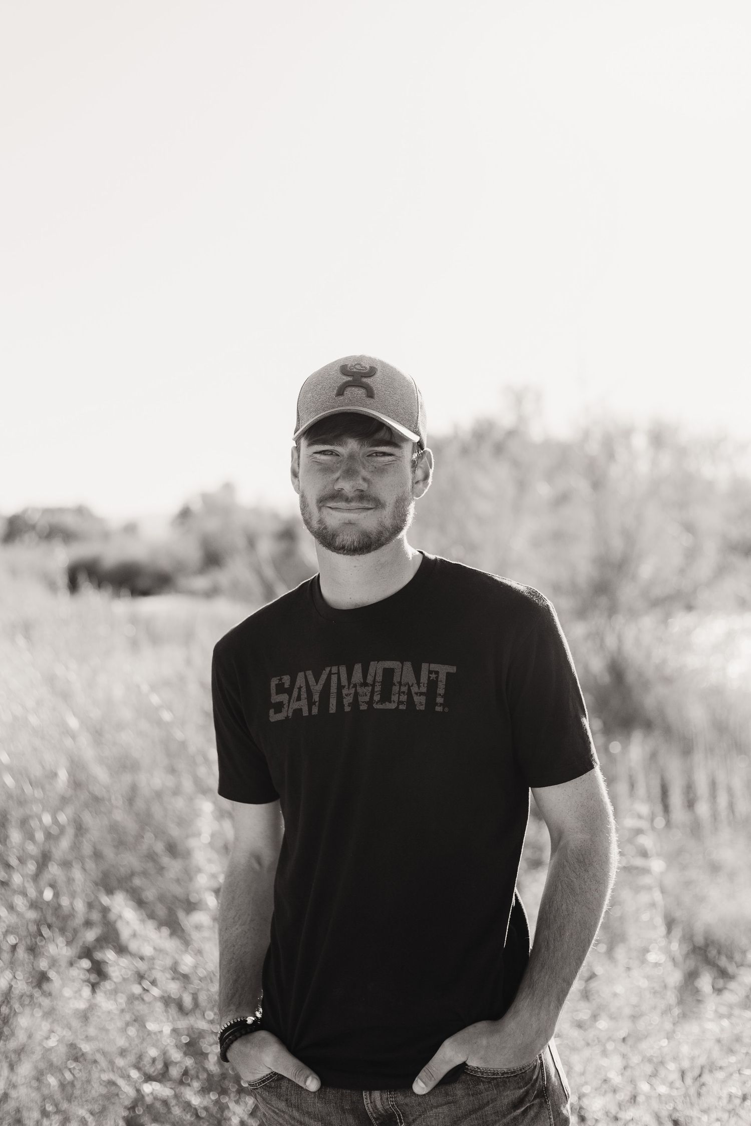Person wearing baseball cap and black t-shirt standing in outdoor field setting.