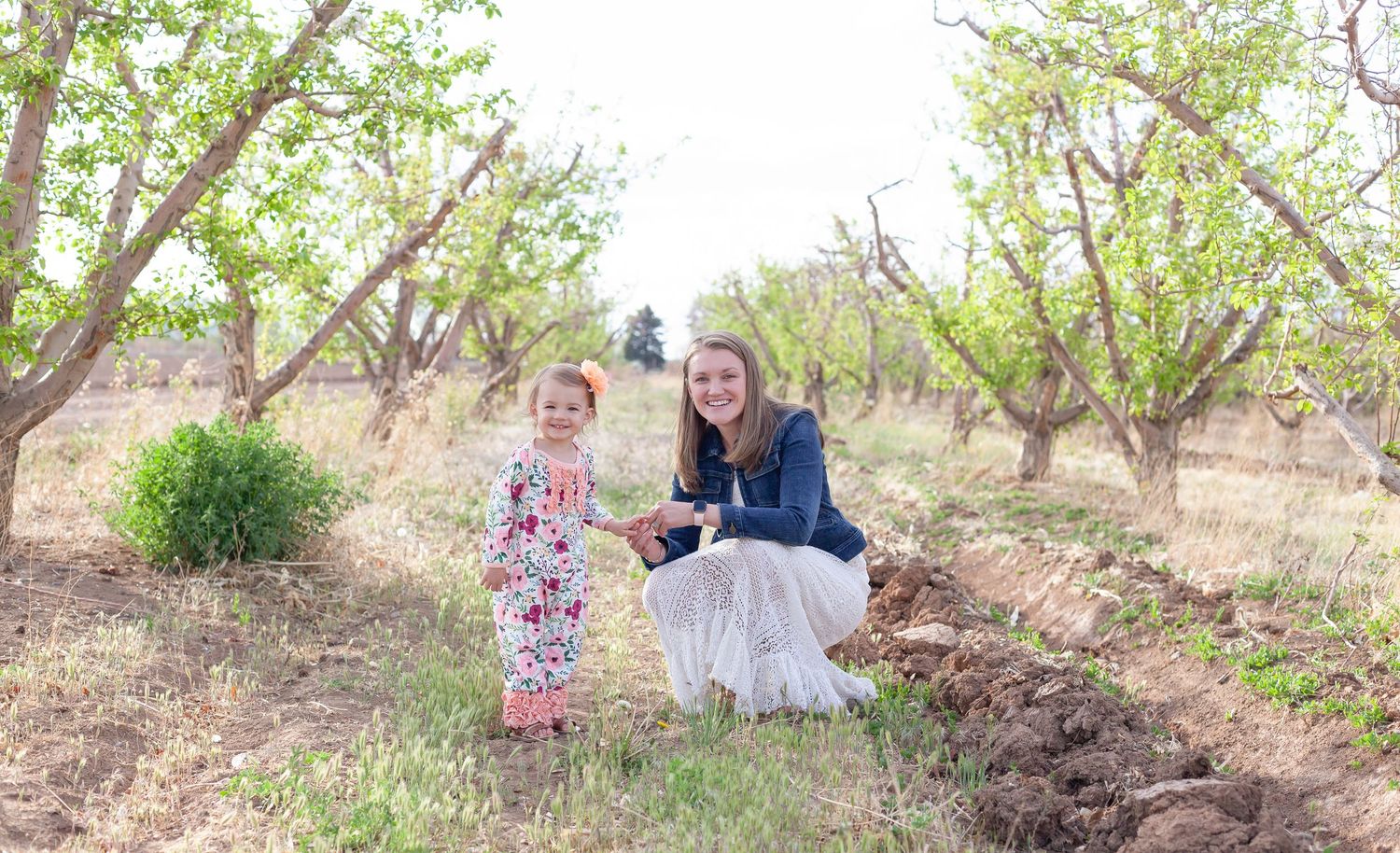 Two people pose together in an orchard during springtime.