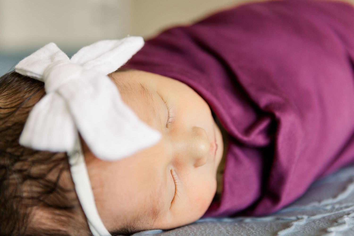 Peaceful sleeping infant with white bow headband against purple fabric.