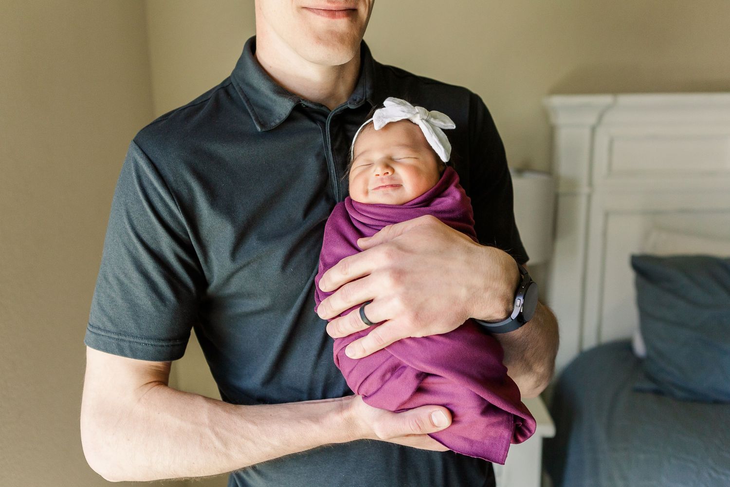 Parent holding newborn baby wearing purple swaddle and white bow.