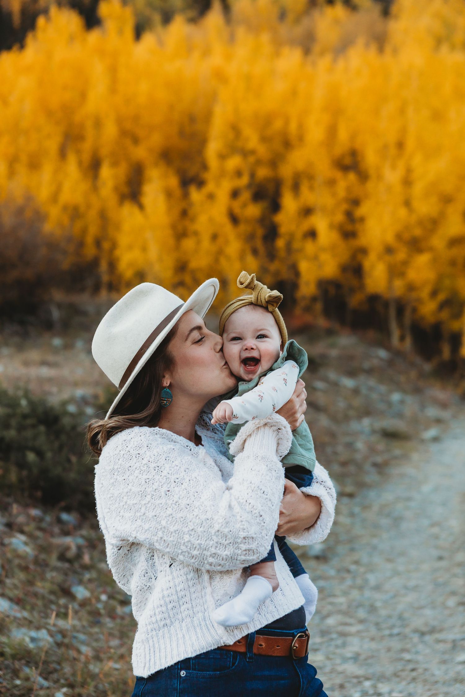 A tender moment shared between parent and child on a hiking trail with vibrant golden autumn trees in the background.