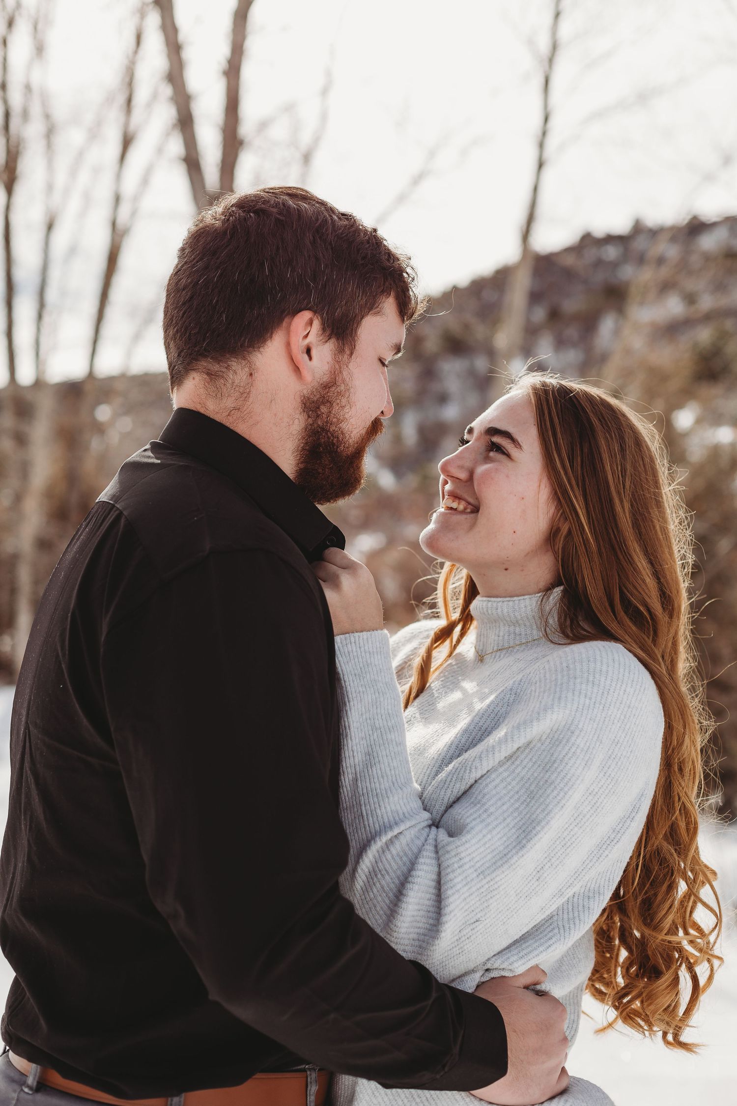 Intimate winter portrait with warm sweaters against a snowy backdrop.