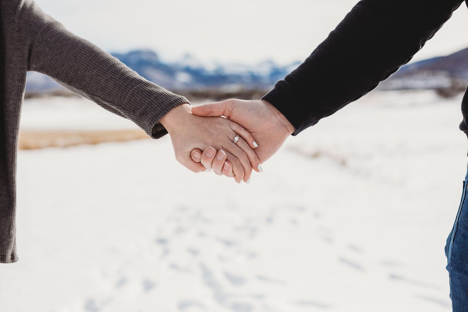 Close-up shot of two people holding hands in a snowy winter landscape.