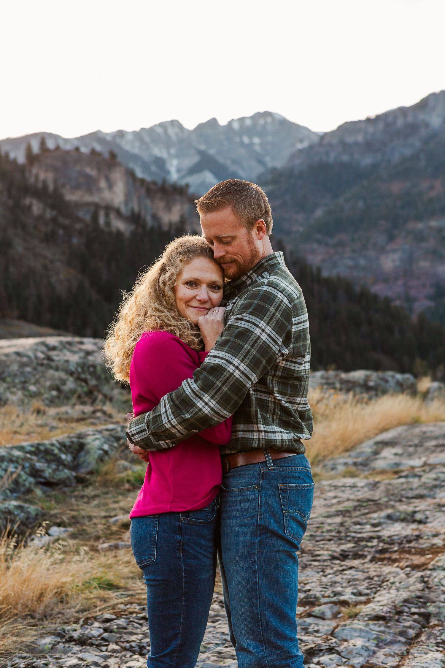 Two people share an intimate moment against a backdrop of majestic mountain peaks during golden hour.
