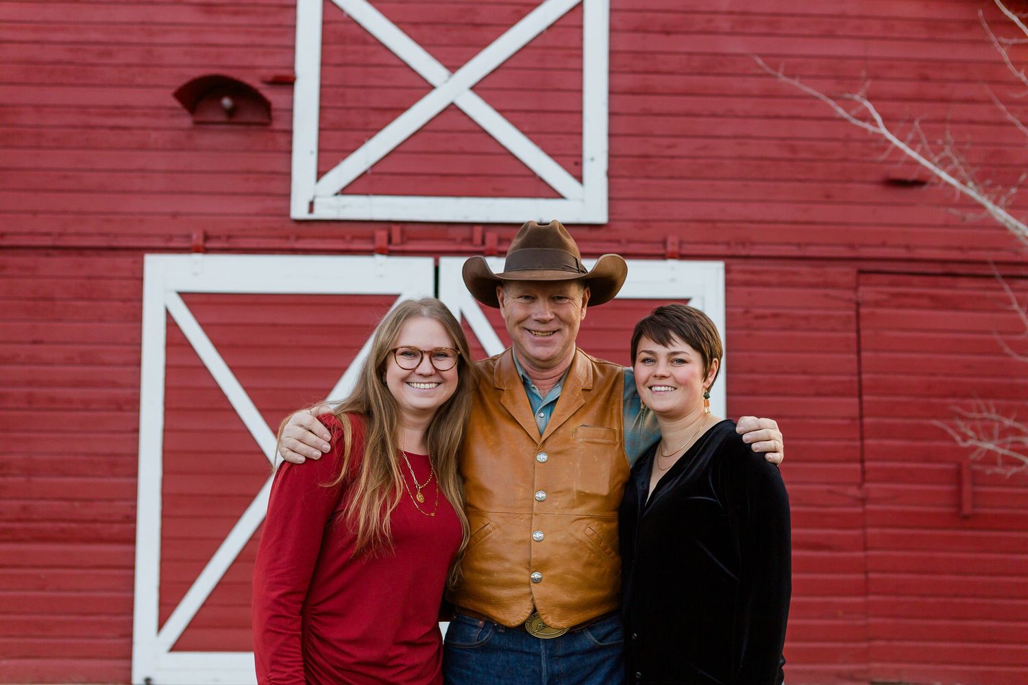 A group poses together in casual attire against a classic red barn with white trim.