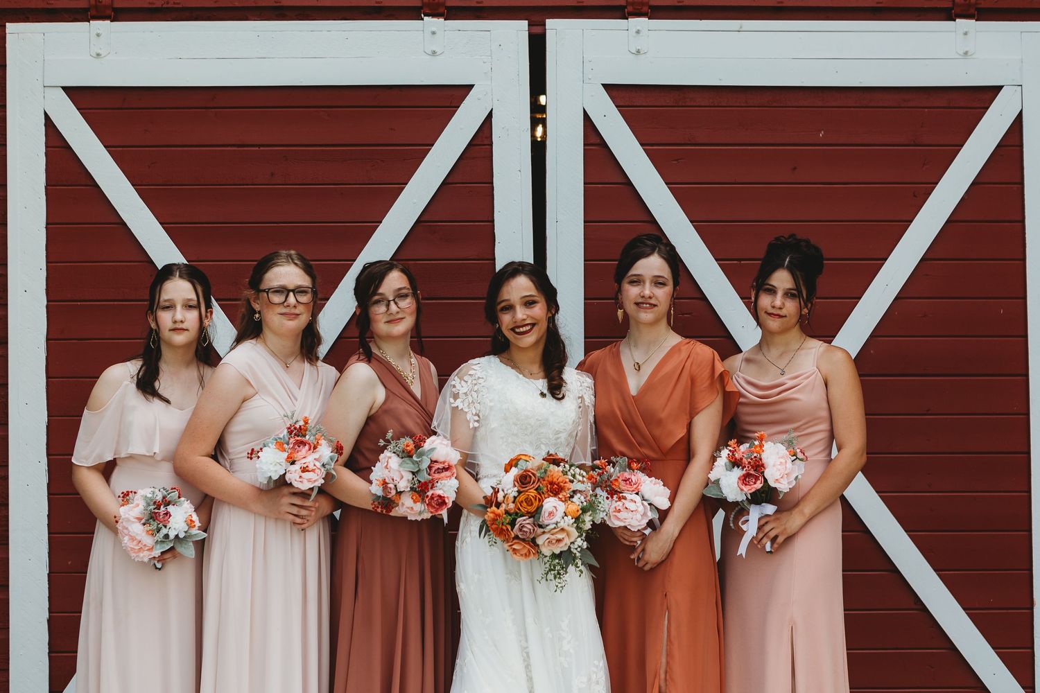 Wedding party in shades of pink and coral poses against red barn backdrop.