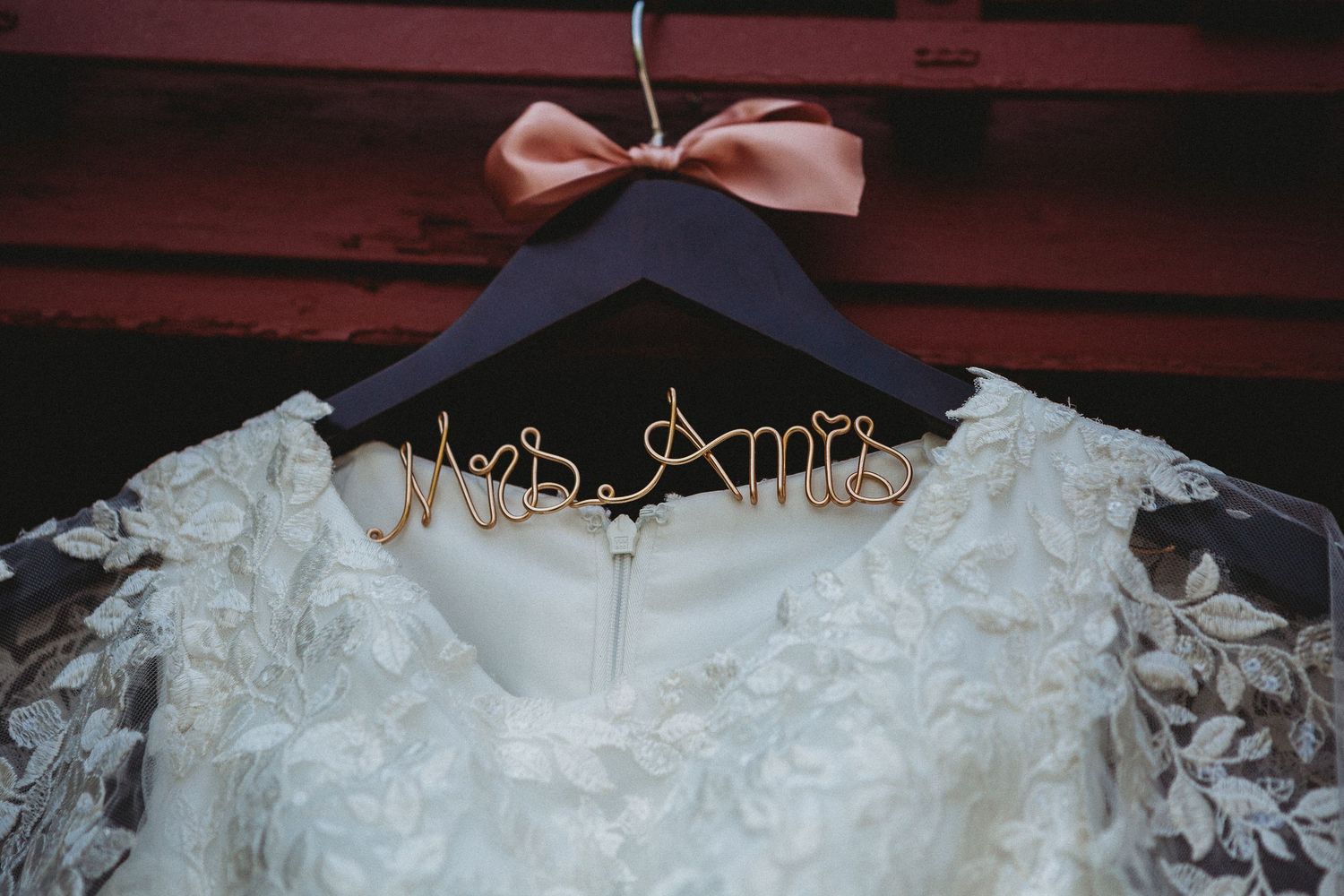 A close-up of a wedding dress hanger with lace details and a pink bow.