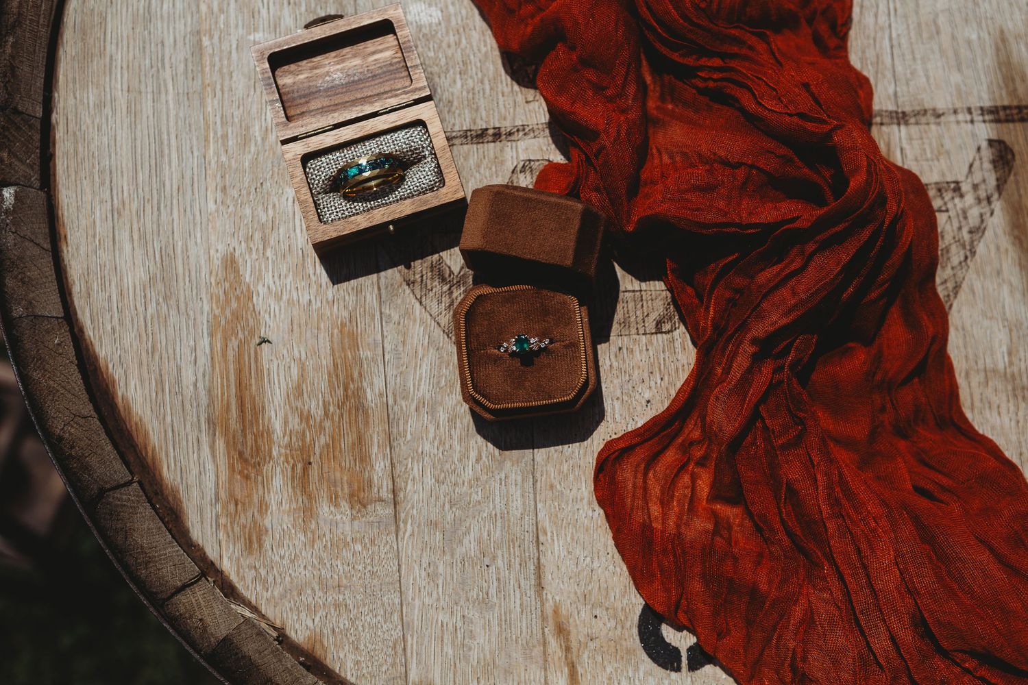Wedding rings in wooden boxes displayed on a rustic wooden surface with red fabric.
