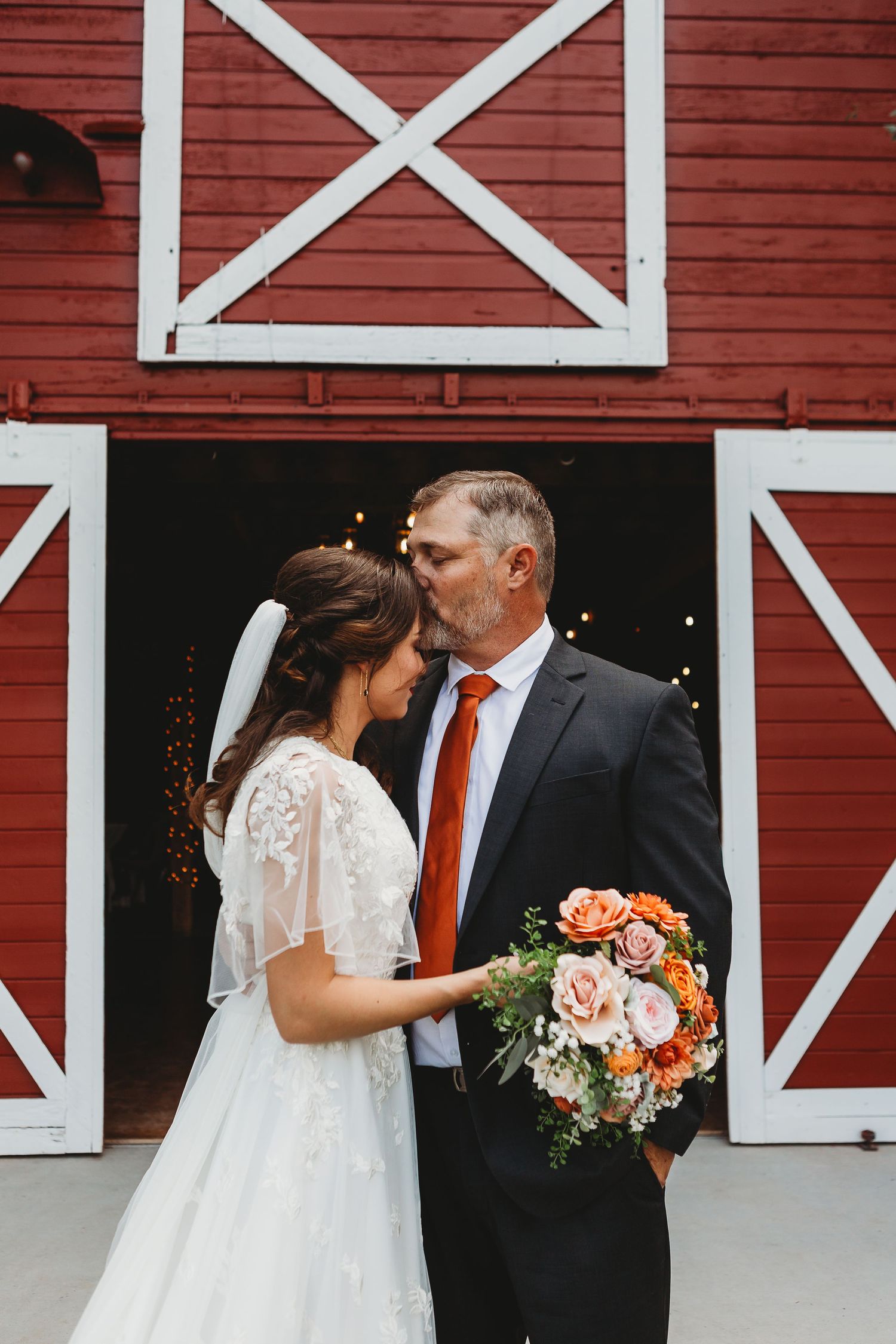 Romantic moment shared in front of red barn doors with white cross detail.