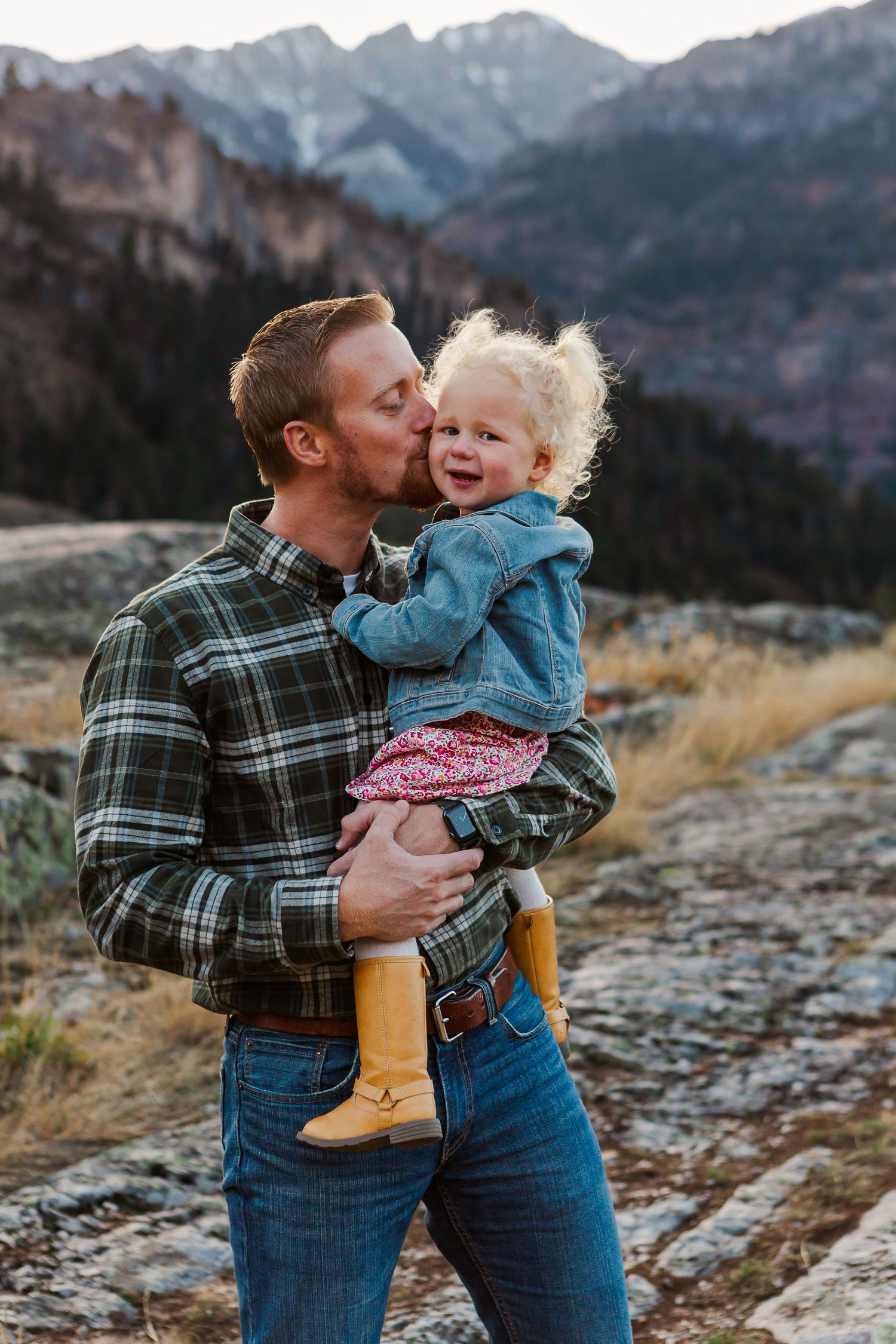 Sweet candid moment captured outdoors with mountain range and autumn scenery in background.
