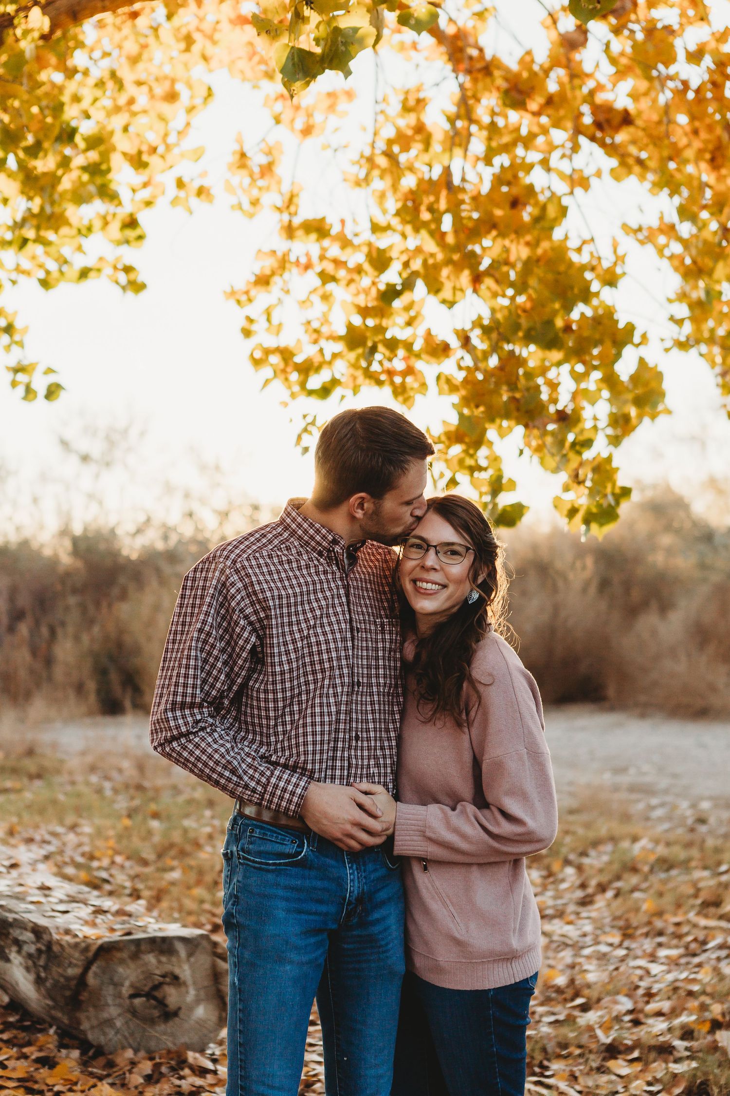 Sweet couple embracing under golden fall foliage near a rustic log.