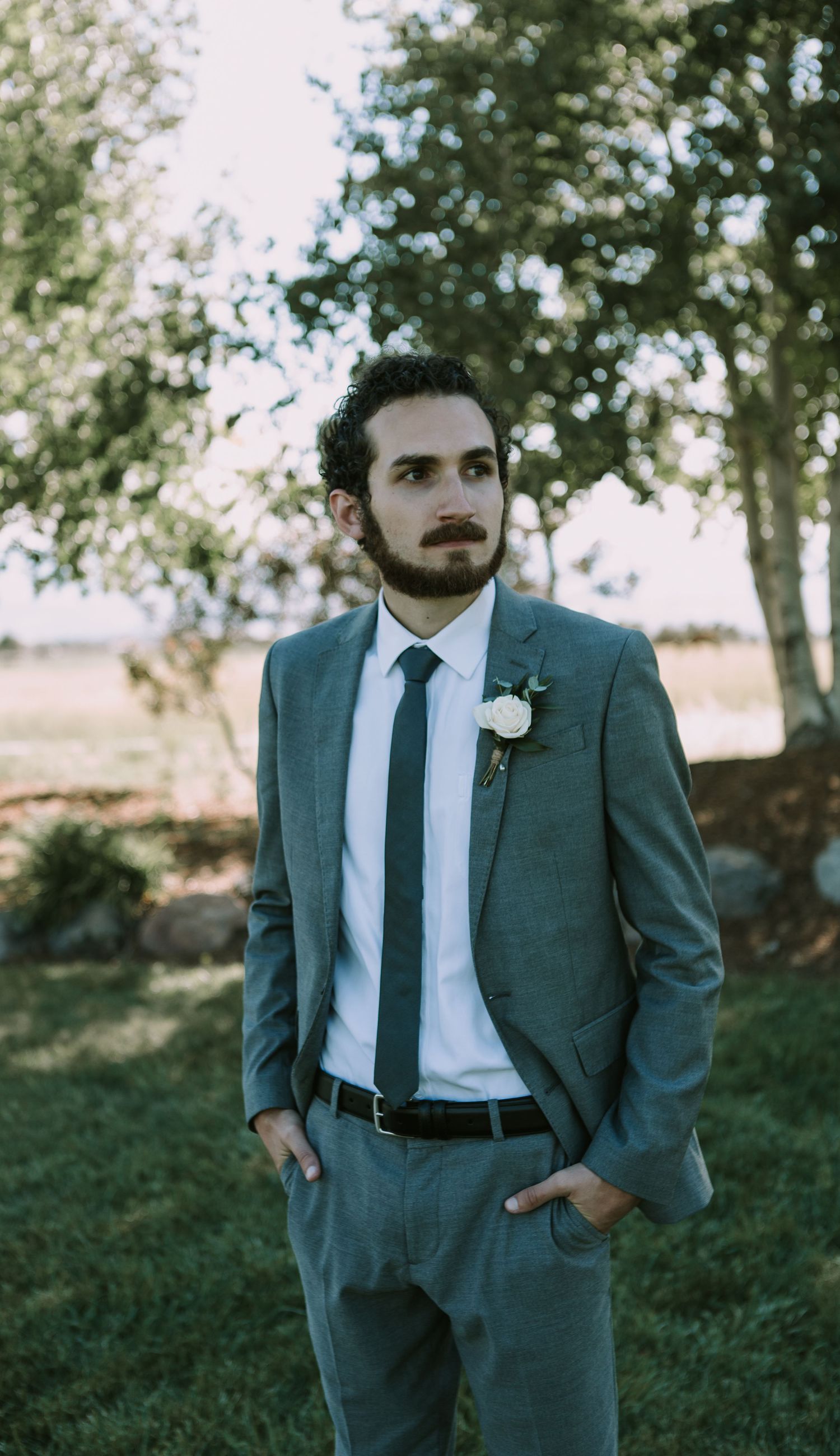 Portrait of groom in tailored gray suit against natural outdoor backdrop.