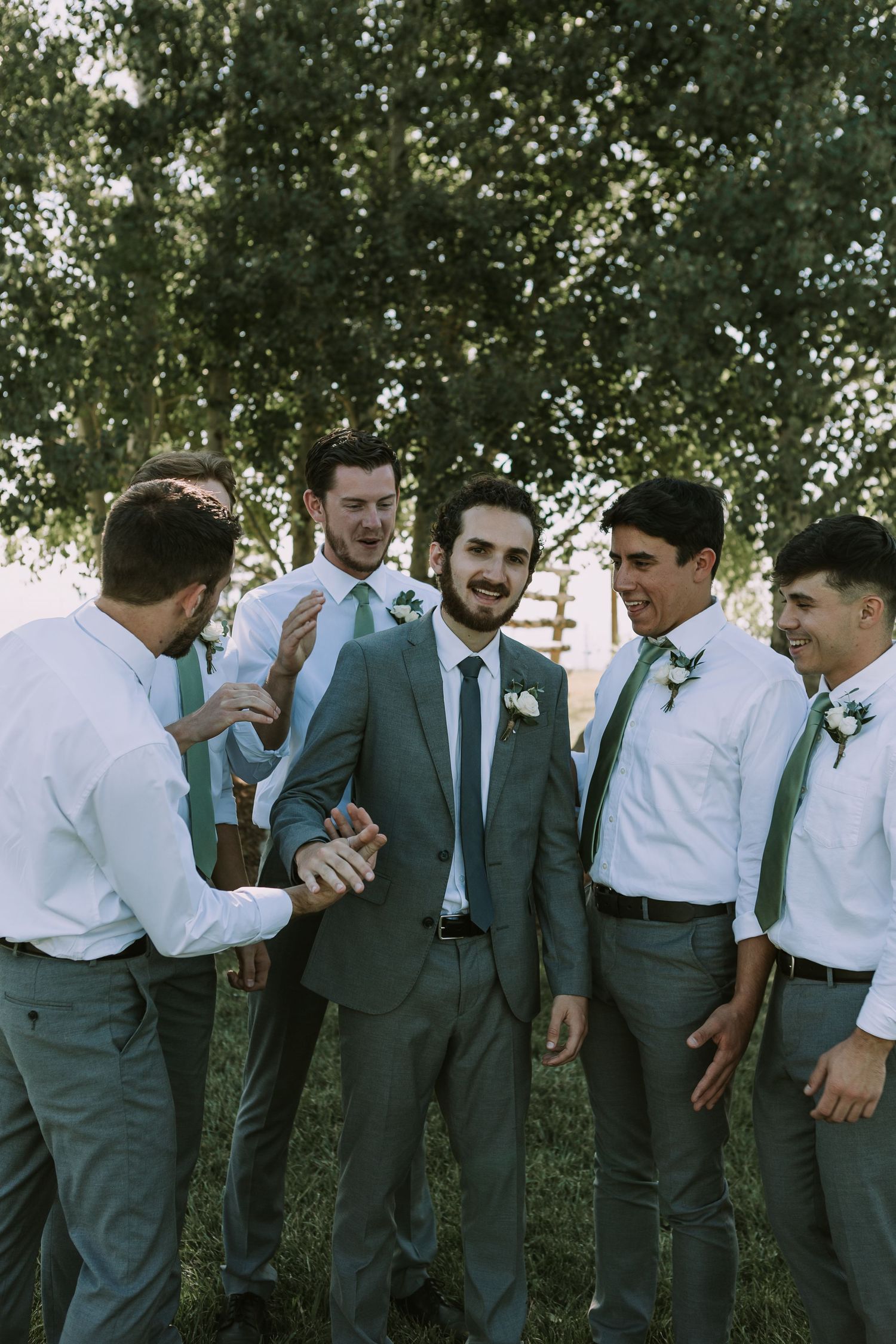 Groomsmen in gray suits and white shirts share a candid moment outdoors.