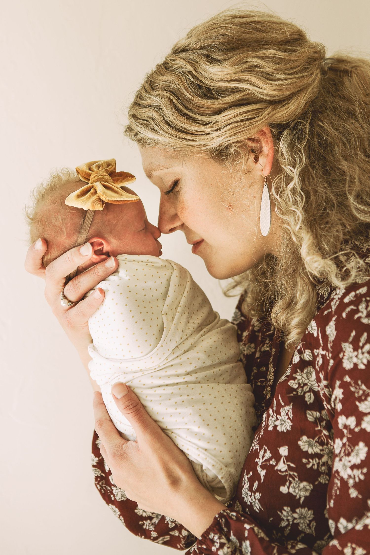 Tender moment with woman in floral dress holding swaddled newborn close.