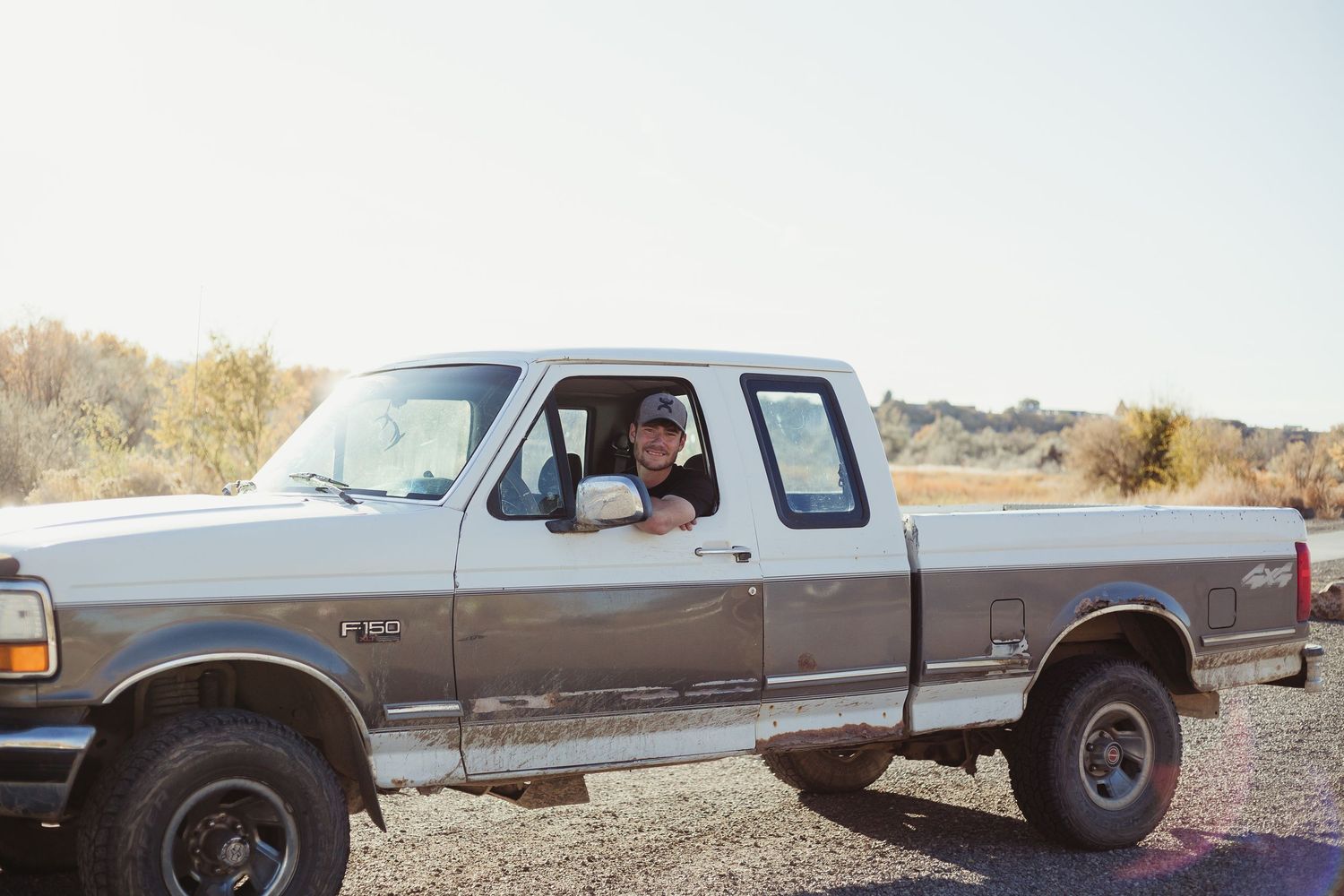 View through truck window of vintage Ford pickup in rural landscape.
