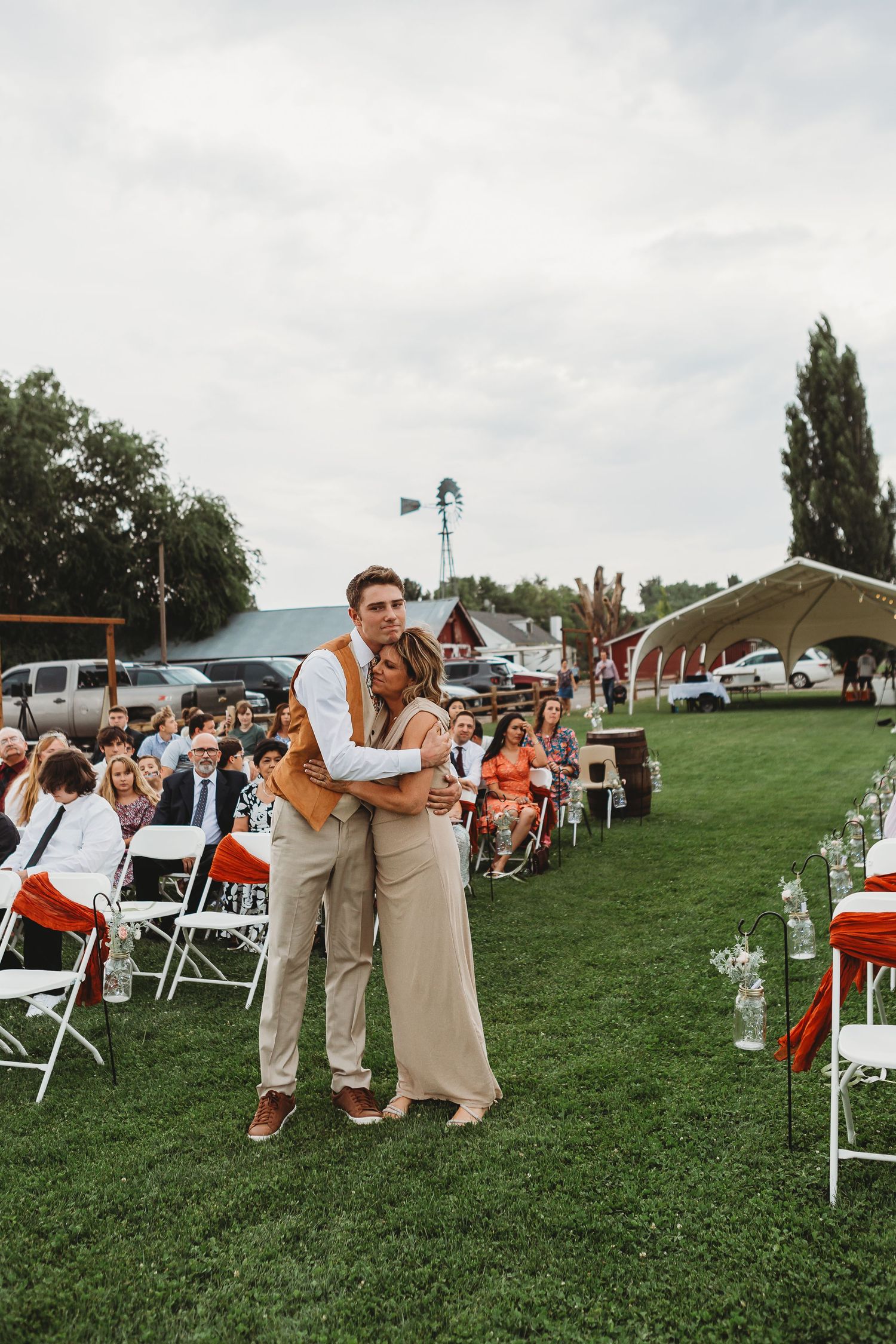 Wedding couple poses together in outdoor ceremony space with white chairs and windmill.