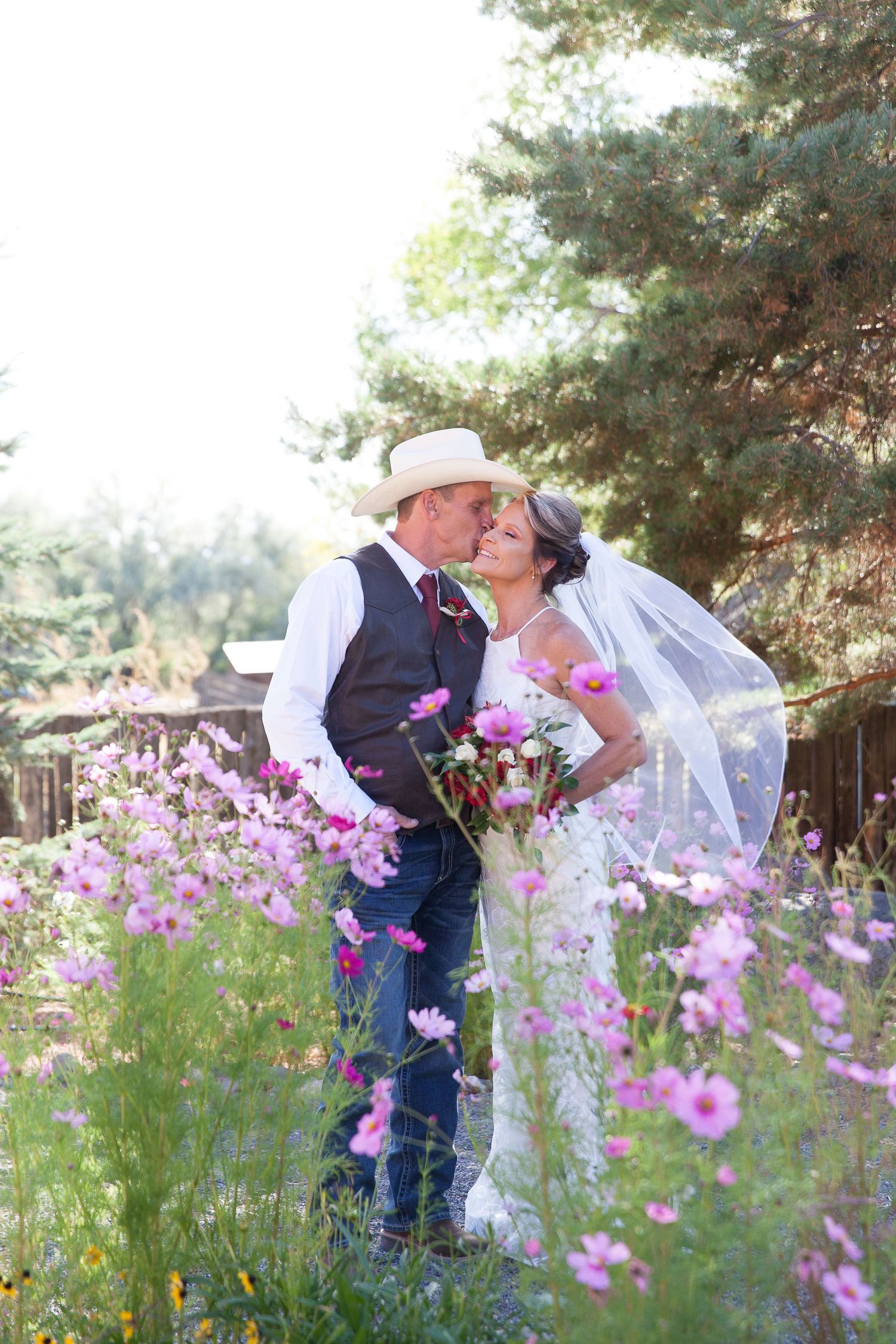 A romantic moment between newlyweds surrounded by blooming purple cosmos flowers in a garden setting.