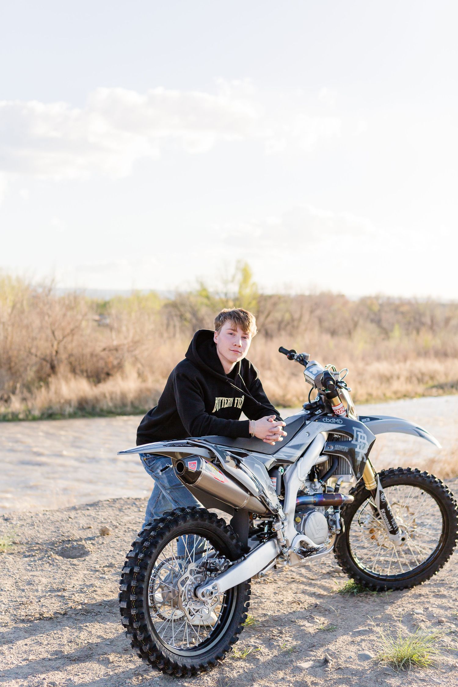 Person sitting on dirt bike on dusty trail during sunny afternoon.