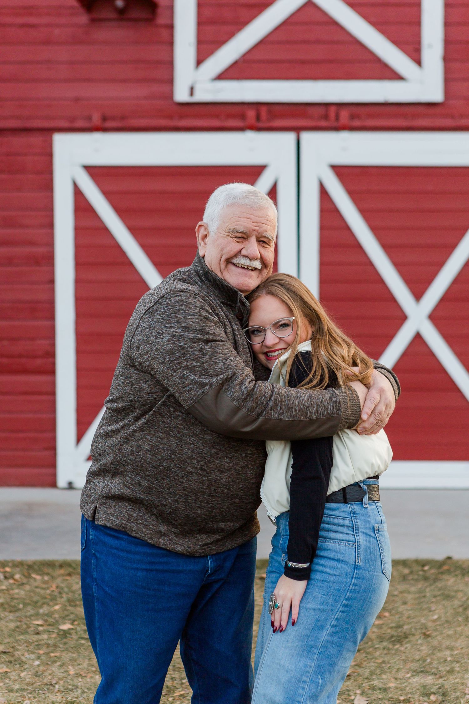 Two people share an affectionate embrace while standing in front of a bright red barn.