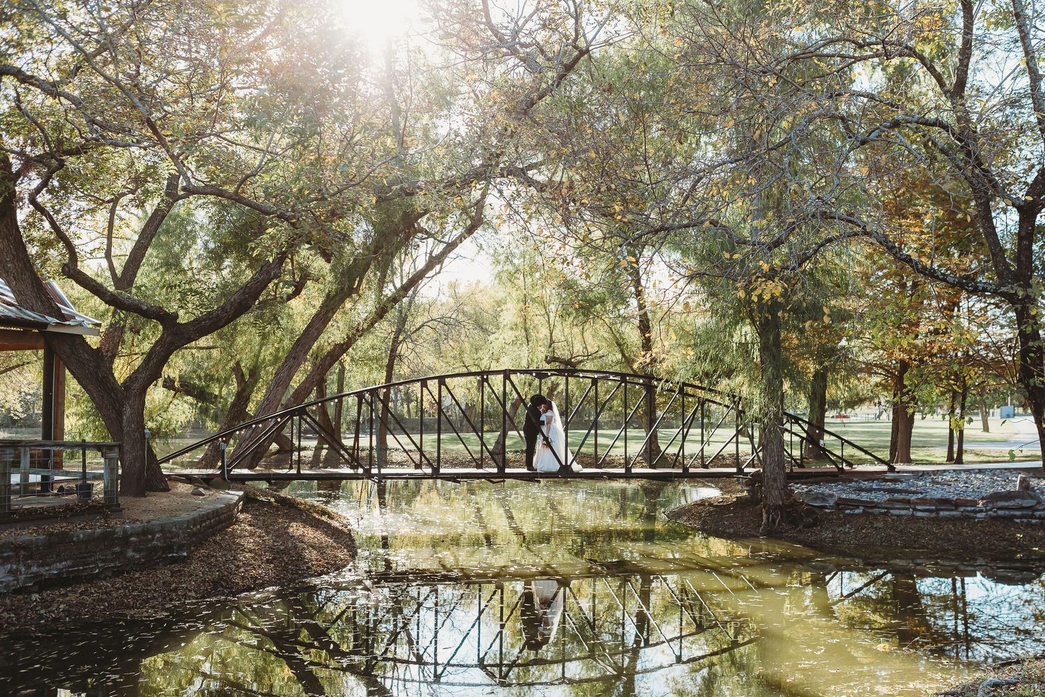 Scenic bridge over reflective pond surrounded by willow trees in golden sunlight.