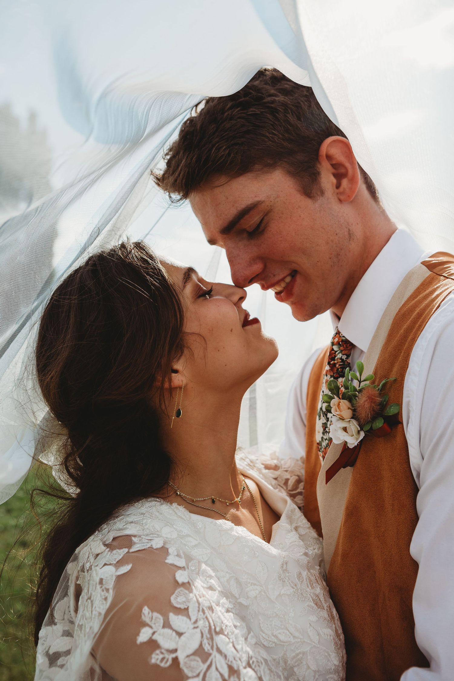 A romantic wedding moment captured under a flowing veil in an outdoor garden setting.