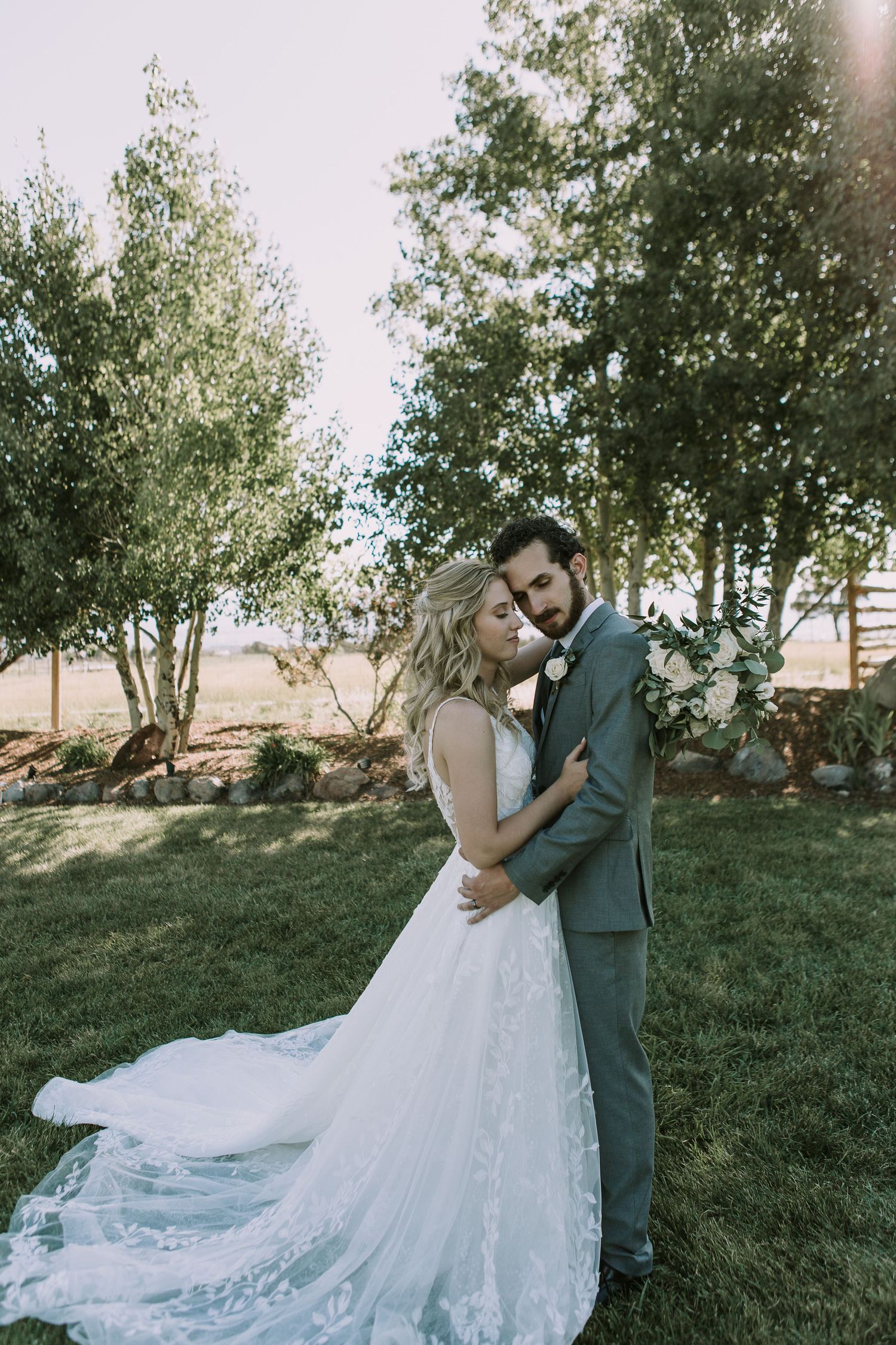 Tender wedding moment photographed in natural setting with stunning lace bridal gown details.