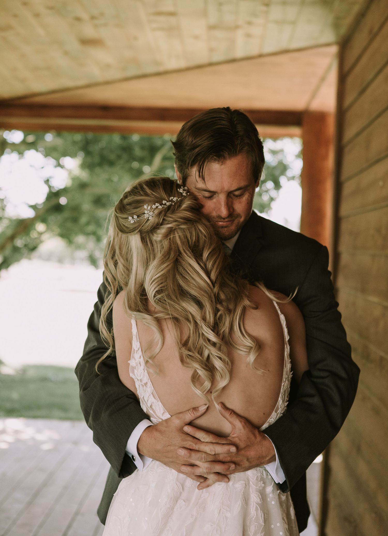 A romantic embrace between couple on rustic porch with bride's flowing curled hair and lace dress.