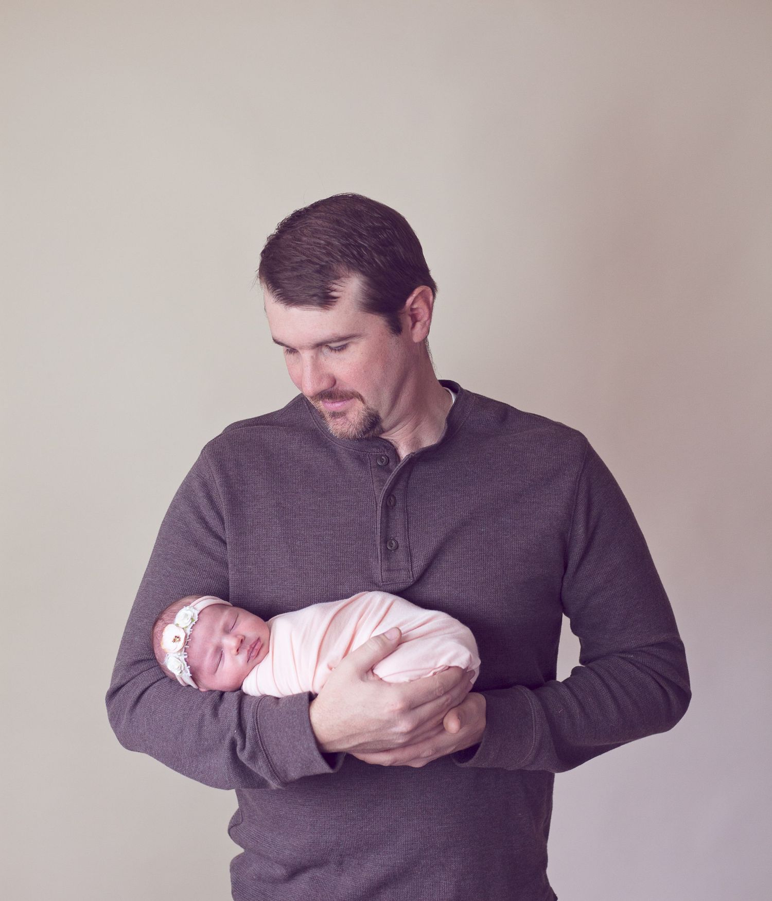 A gentle moment with father holding a swaddled newborn baby in studio lighting.