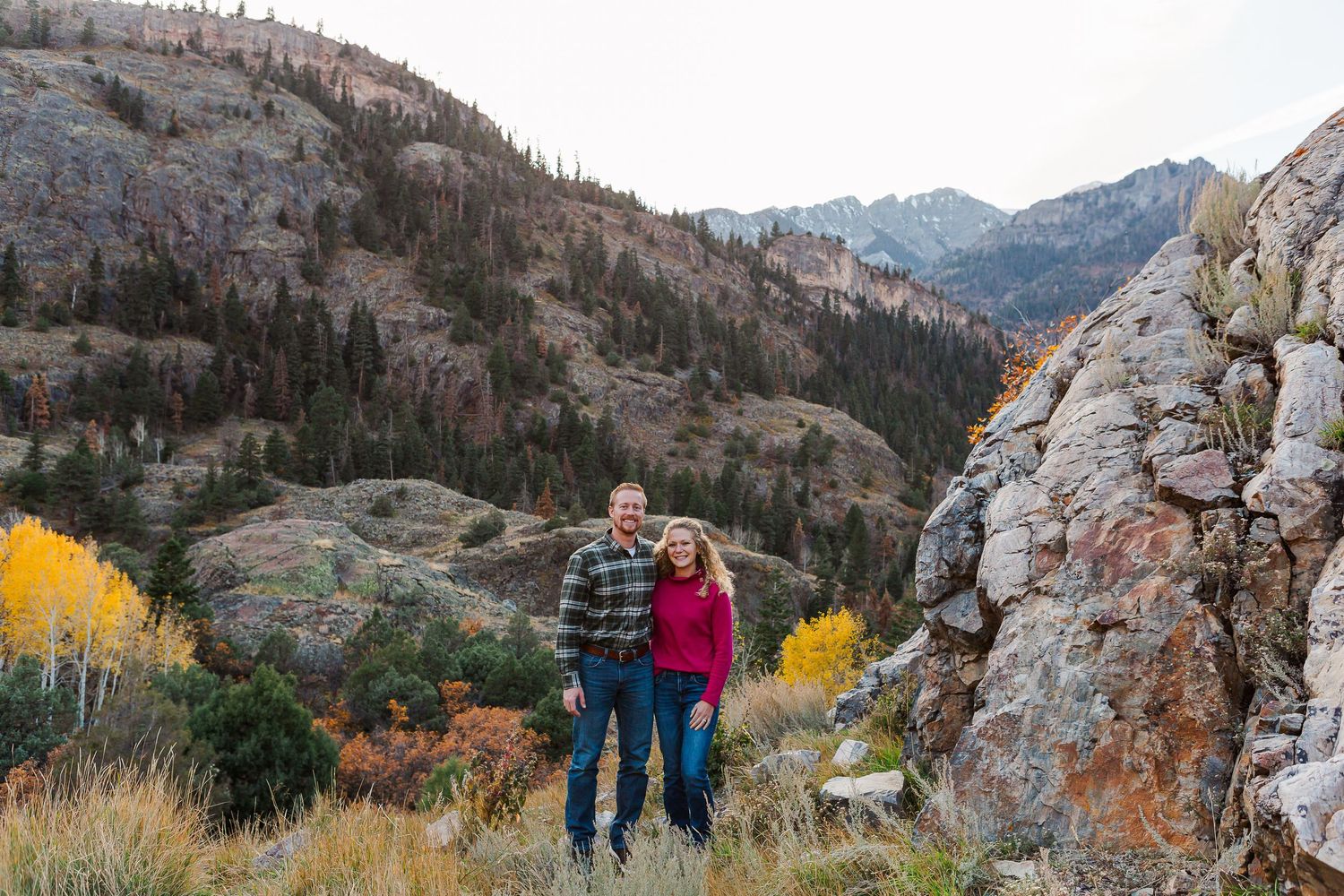 Mountain vista with couple standing near large rock formation during fall season.