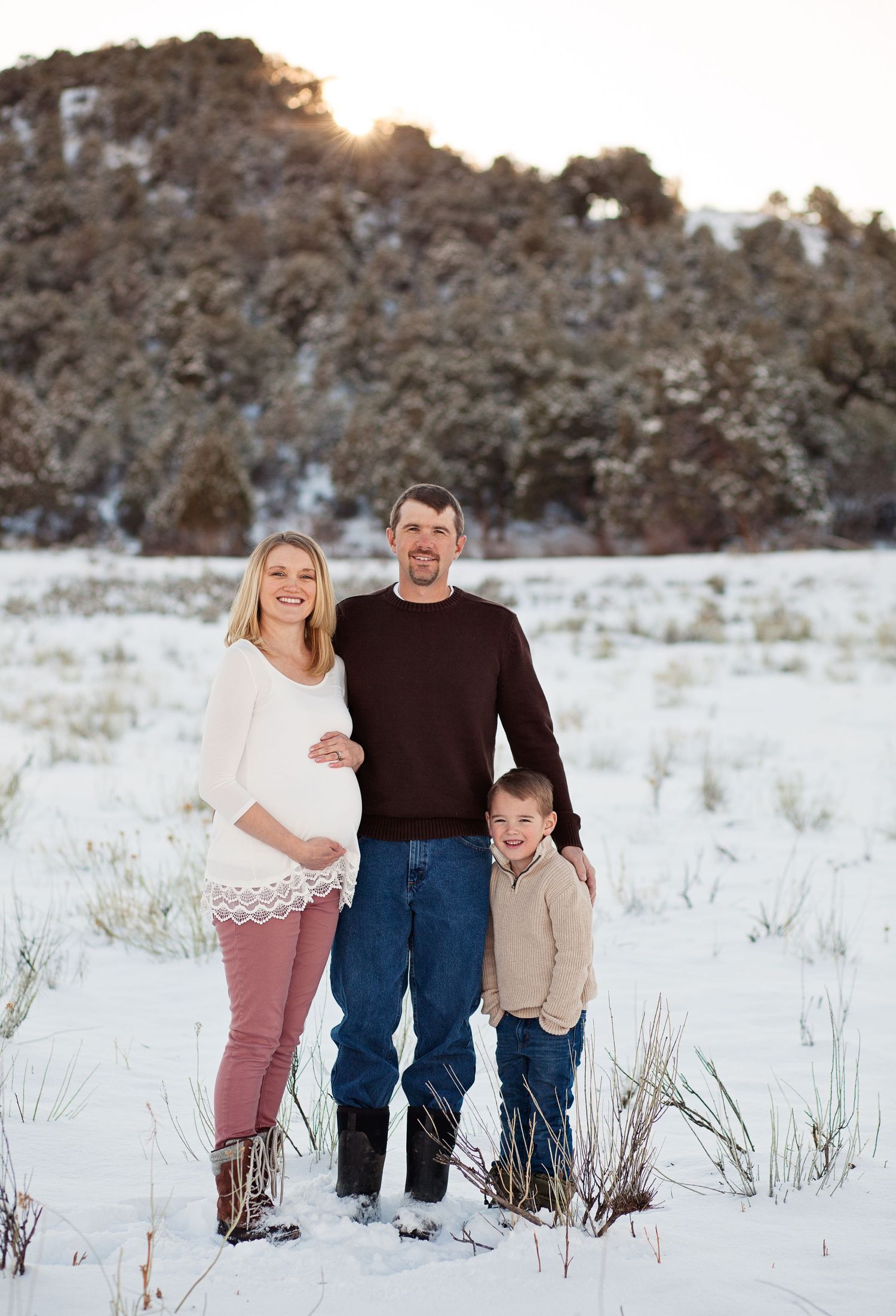 Family winter portrait in snow with rocky mountain landscape at sunset.