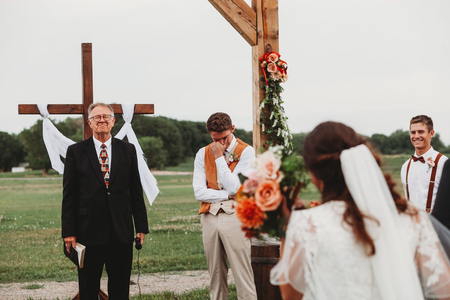Wedding ceremony taking place under wooden arch with rustic decor.