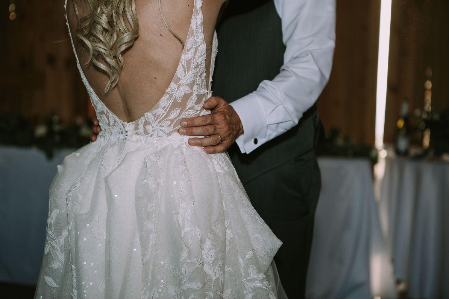 Close-up detail of a lace wedding dress back with hands embracing during a romantic moment.