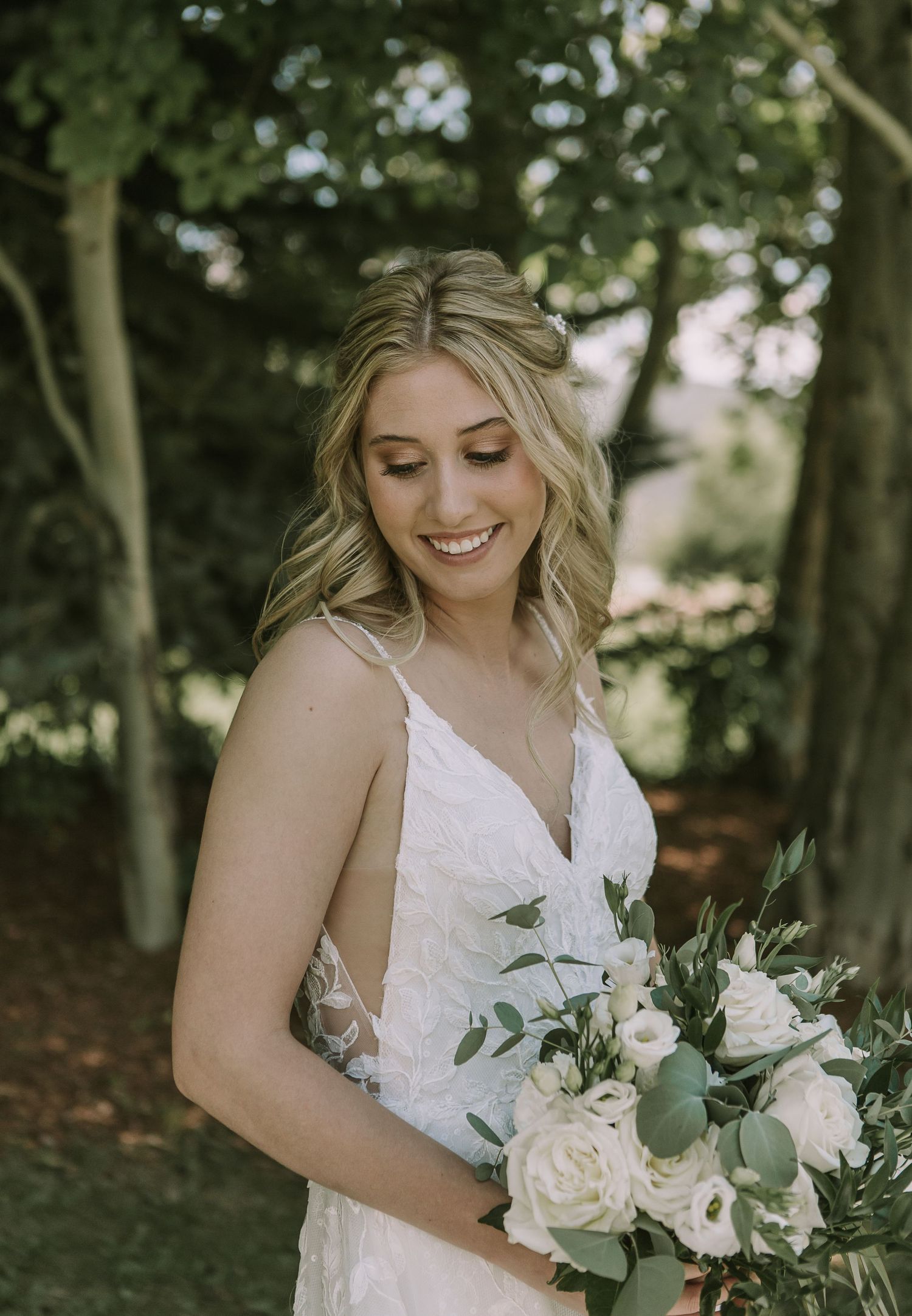 Bride in v-neck lace gown smiles while holding elegant white and green bouquet.
